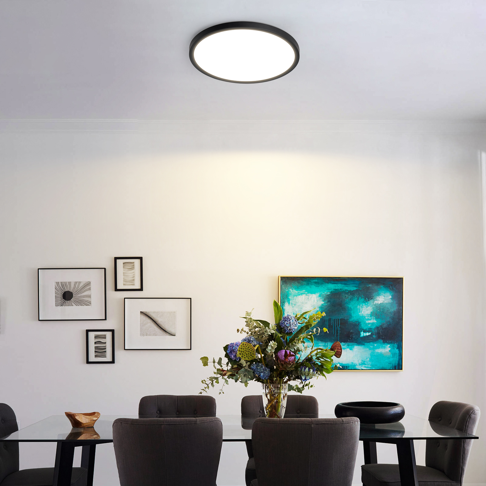 Comedor con luz de techo negra, arte y una mesa de cristal con flores. Sillas grises.