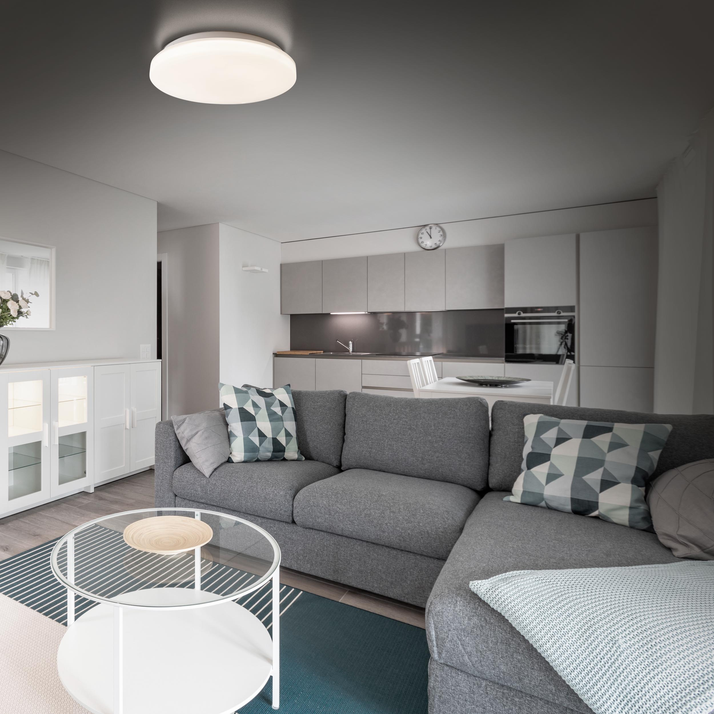 Wohnzimmer mit grauem Sofa, Glas-Couchtisch und einer weißen Deckenleuchte.