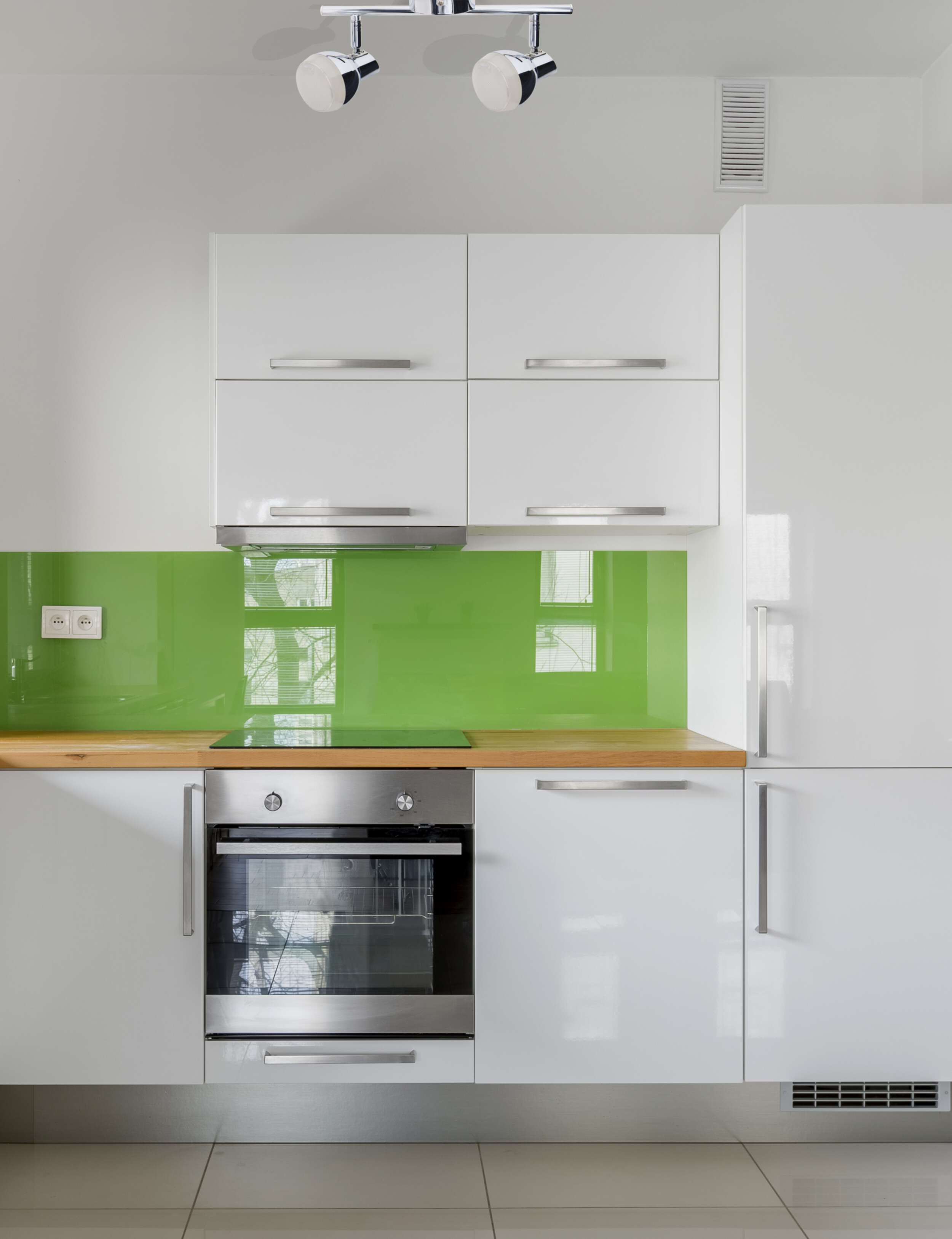 Eine moderne Küche mit weißen Schränken, einem grünen Fliesenspiegel und einem Edelstahlbackofen.