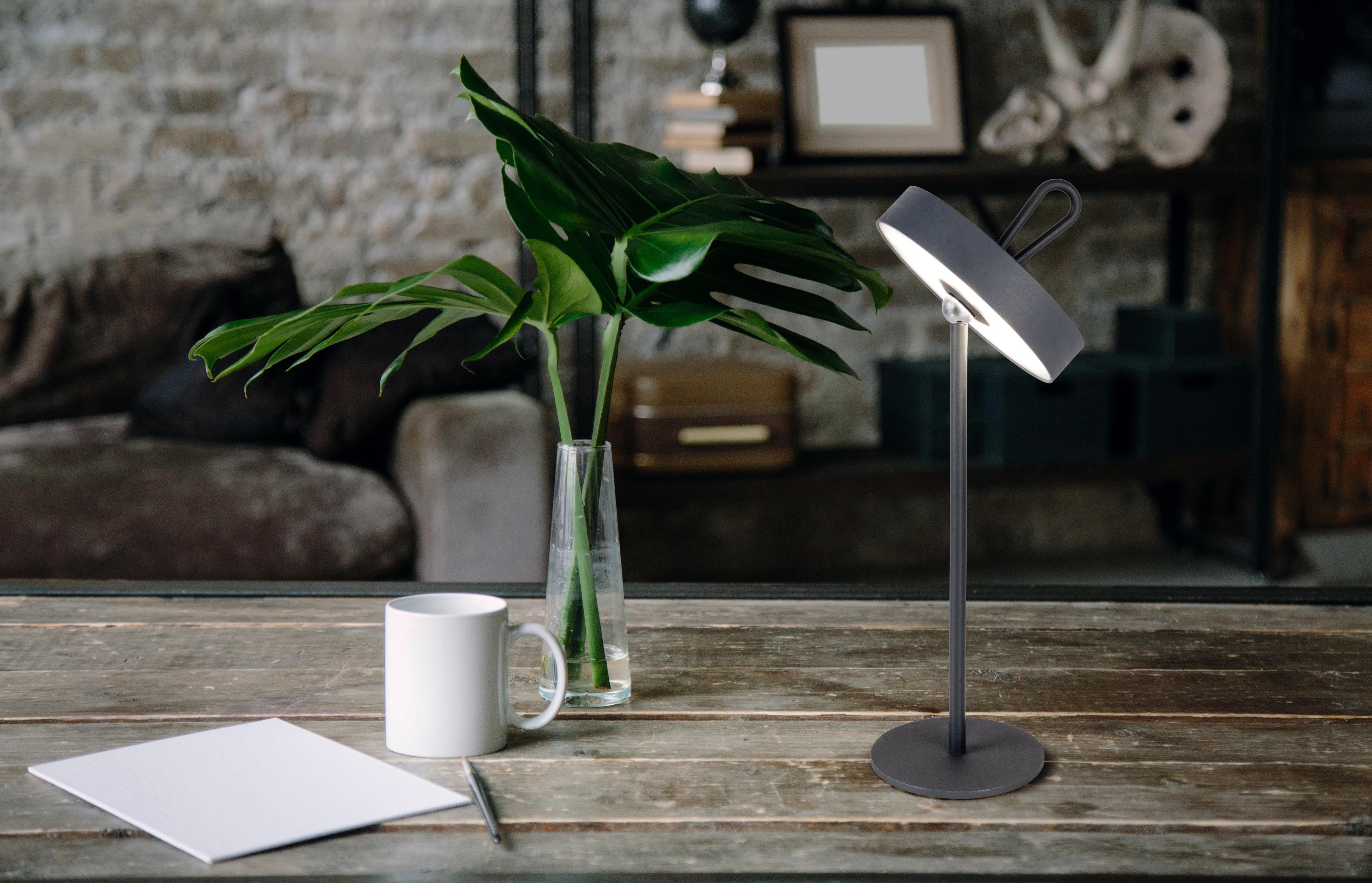 Eine moderne Schreibtischlampe mit einem gebogenen Leuchtenkopf und einer weißen Tasse und einer Pflanze auf einem Schreibtisch.