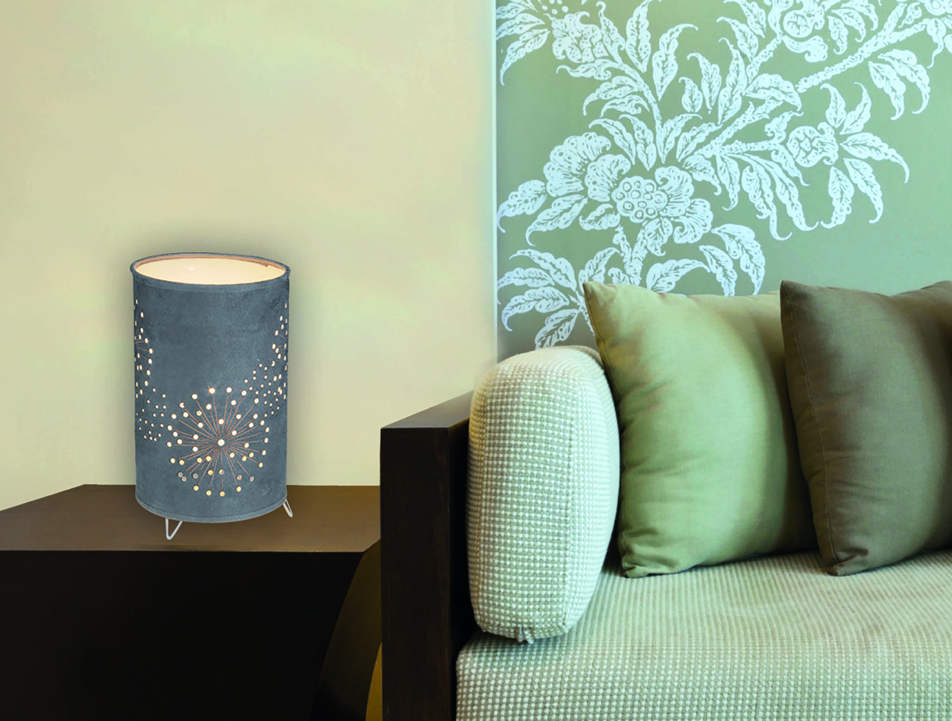 Graue Tischlampe mit Aussparungsdesign, emittiert warmes Licht, neben einem Sofa mit Kissen.
