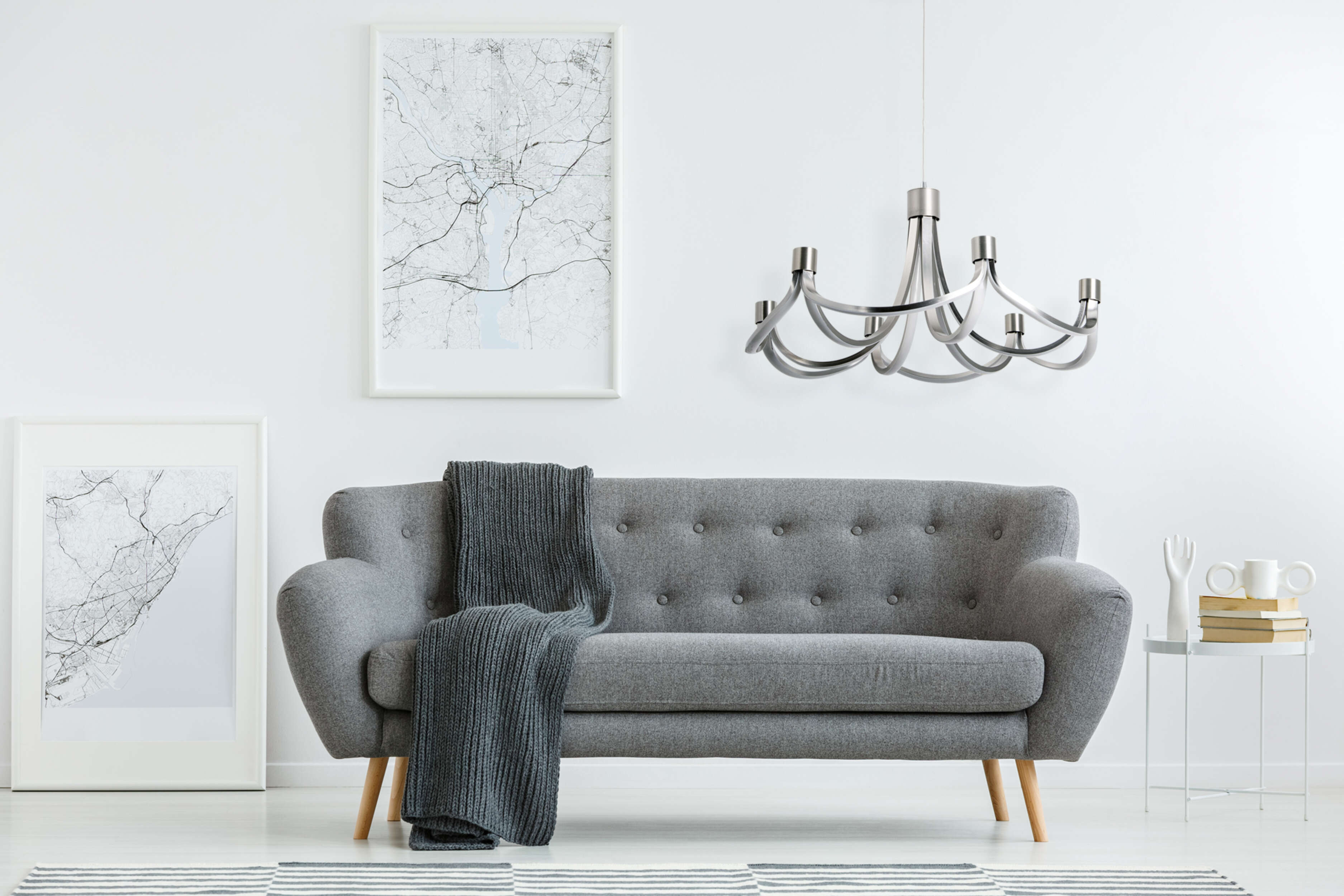 Ein Rauminnenraum mit grauem Sofa, Bildern und moderner Kronleuchterbeleuchtung.