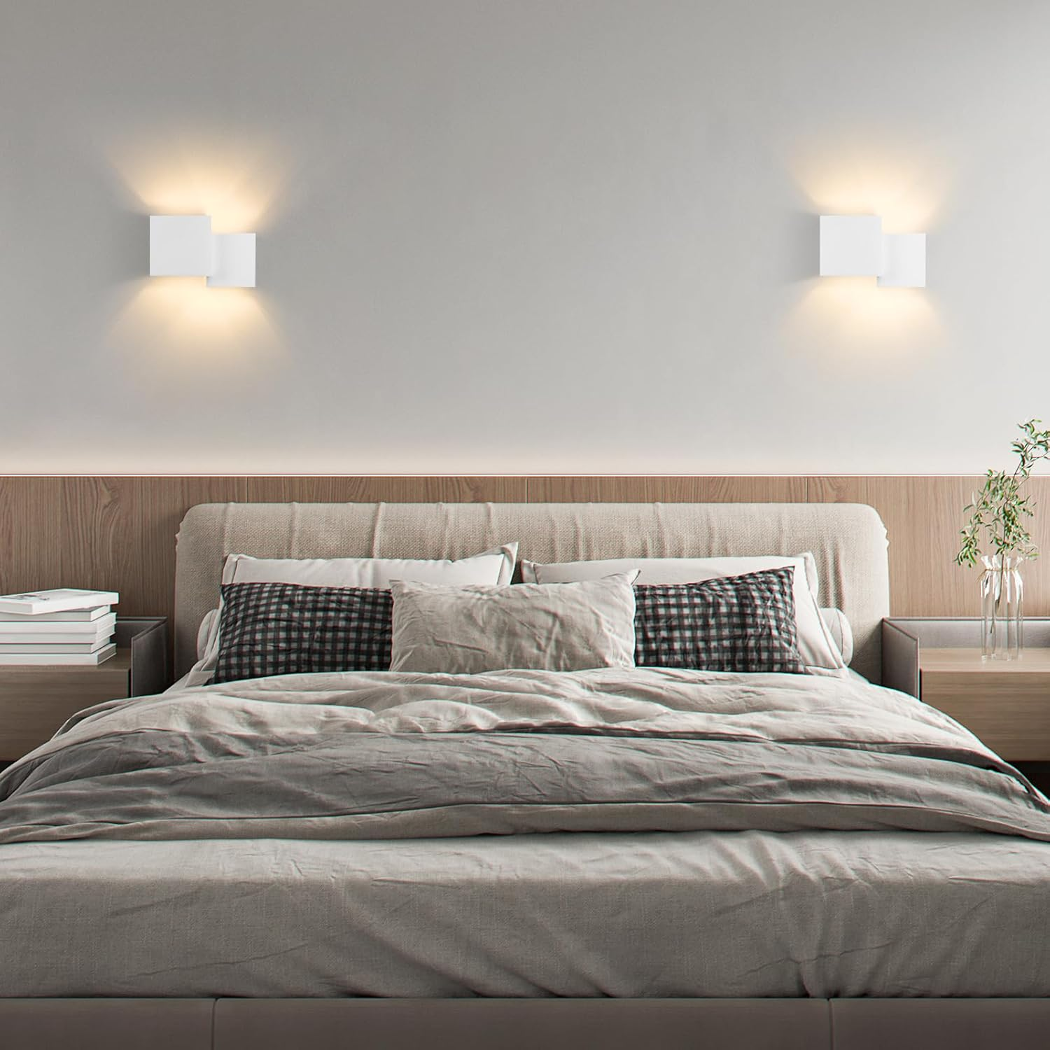 Dos apliques de pared cuadrados blancos, que iluminan una cama con almohadas y una planta sobre una mesa.
