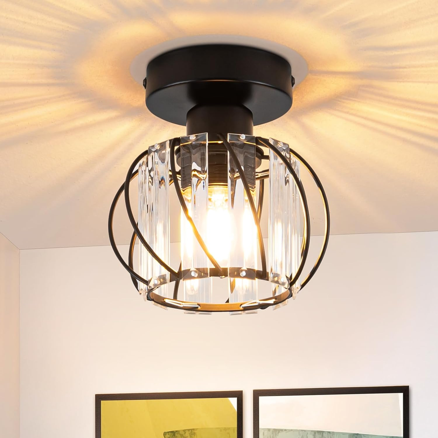 Czarna lampa sufitowa ze szklanym cylindrem wokół żarówki. Jest zamontowana na białym suficie.