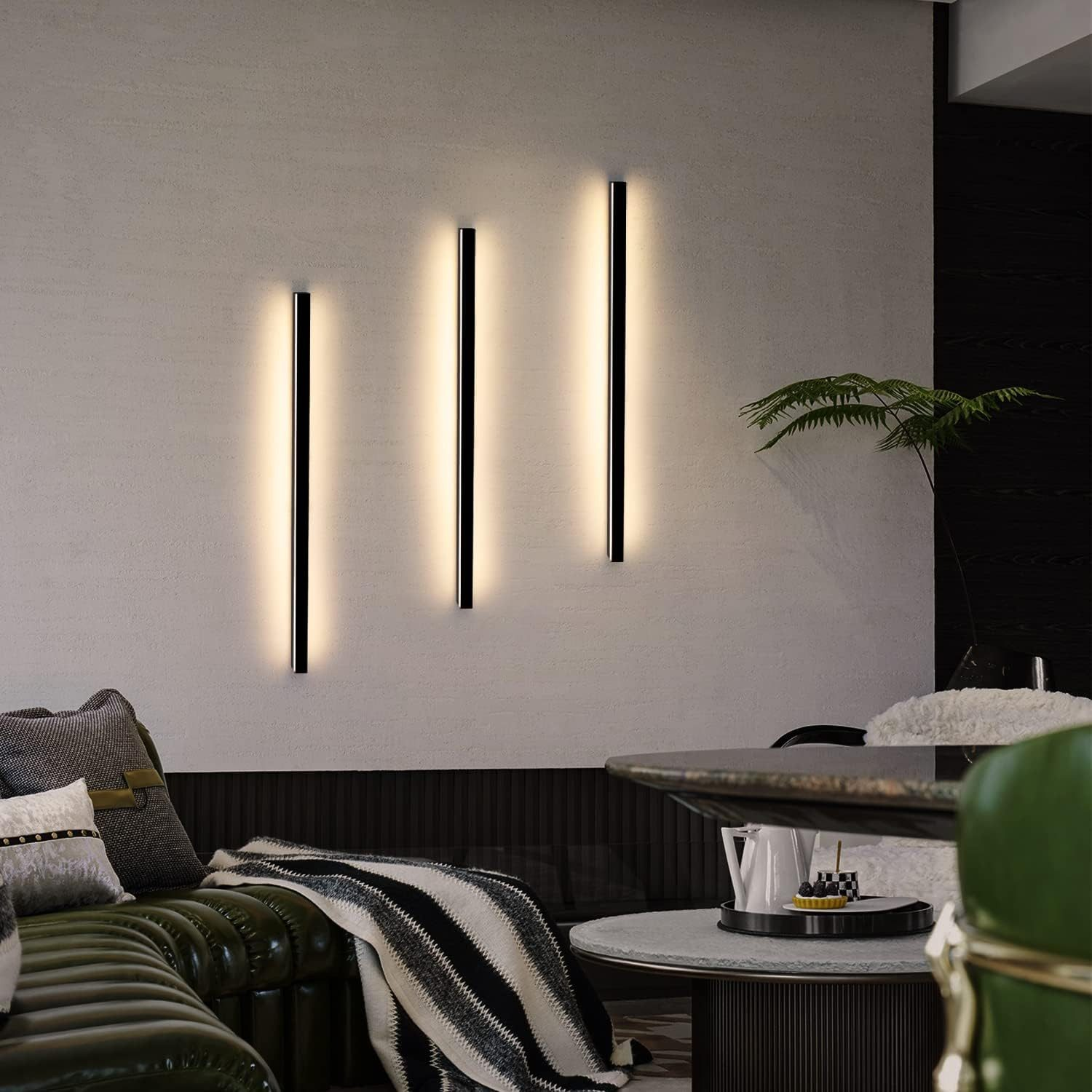 Tre luci LED verticali nere su una parete grigio chiaro. Un tavolo e un divano sono nella scena.