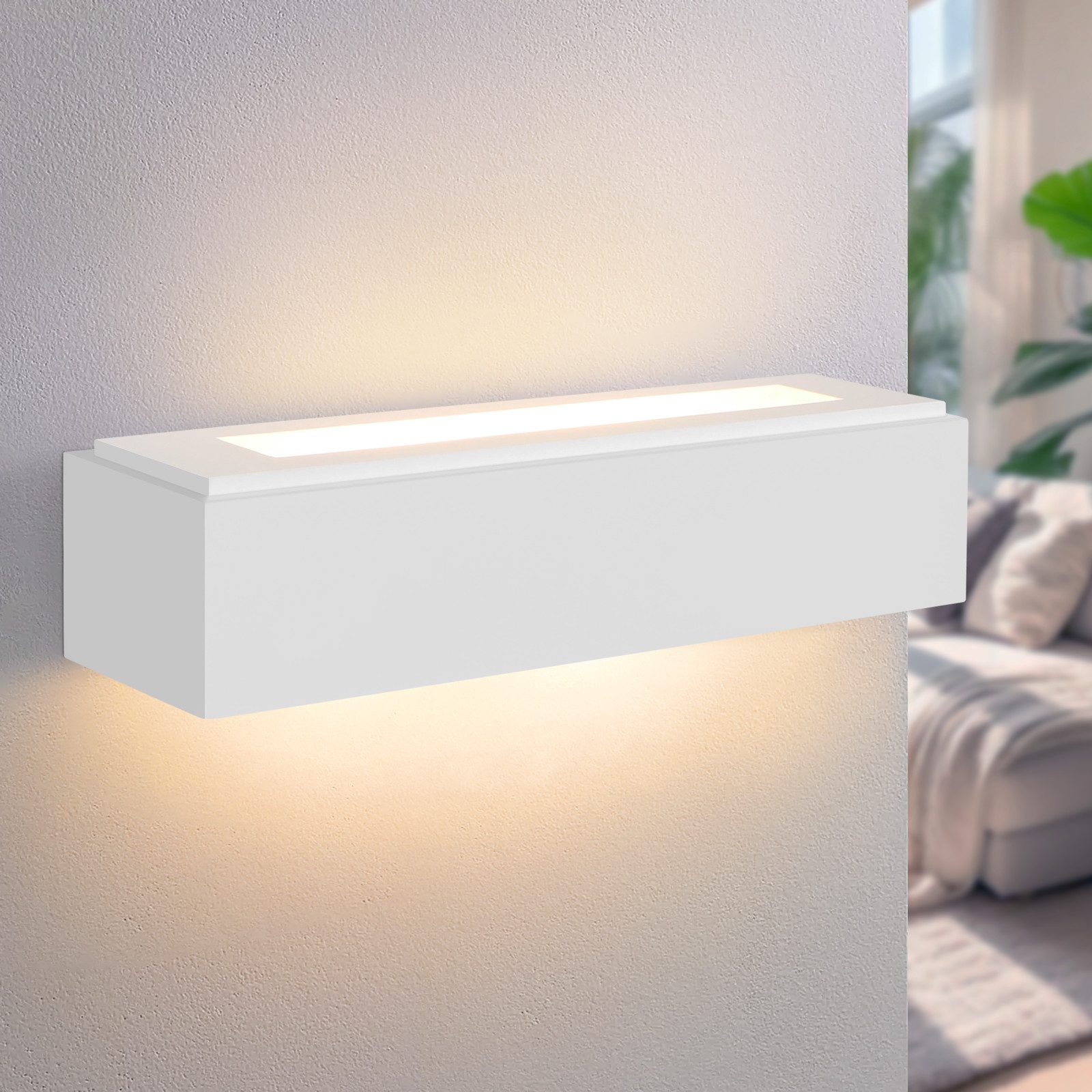 Una luce da parete rettangolare bianca montata su un muro bianco. Emette luce verso il basso.