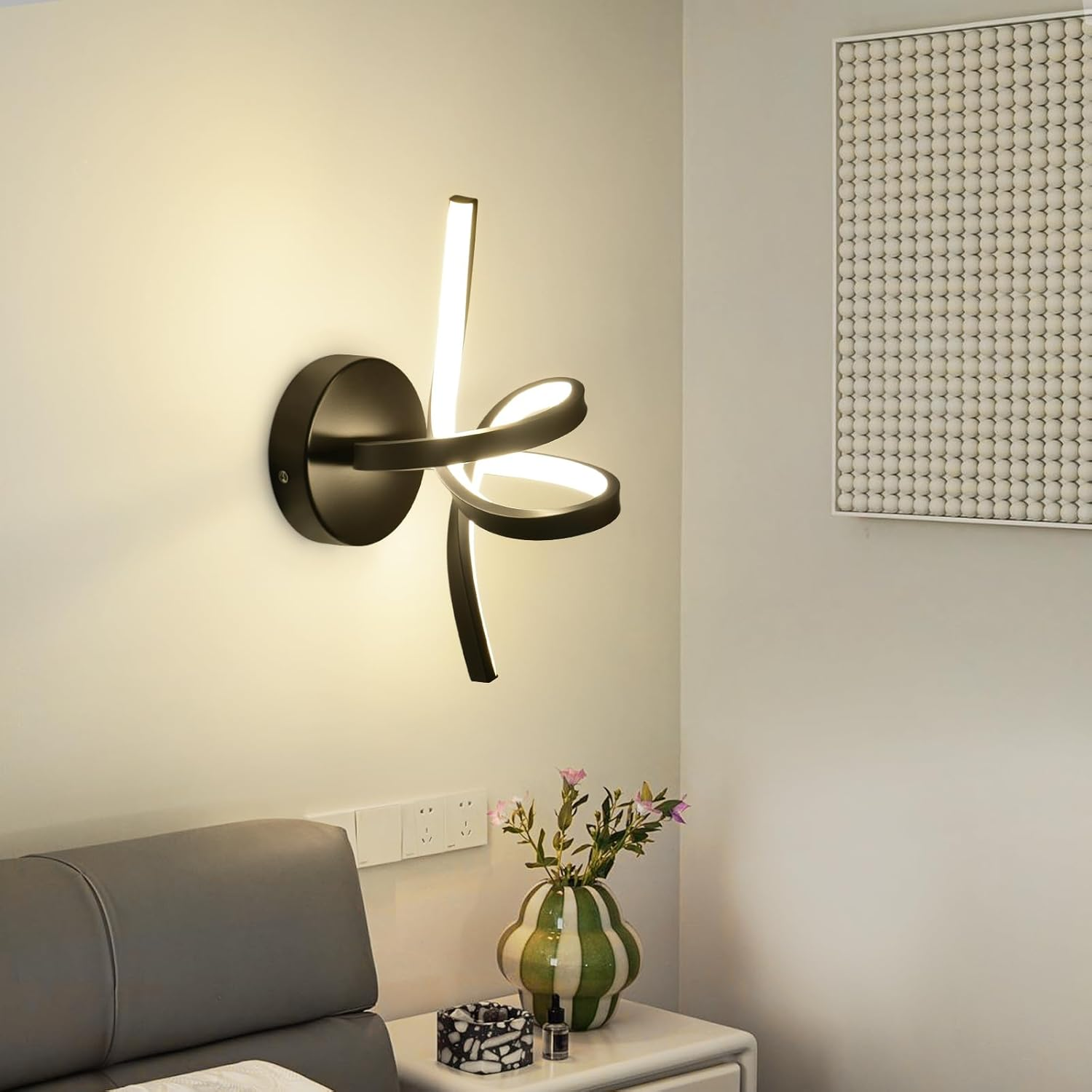 Lampada da parete nera con base circolare e bracci curvi illuminati su muro beige.