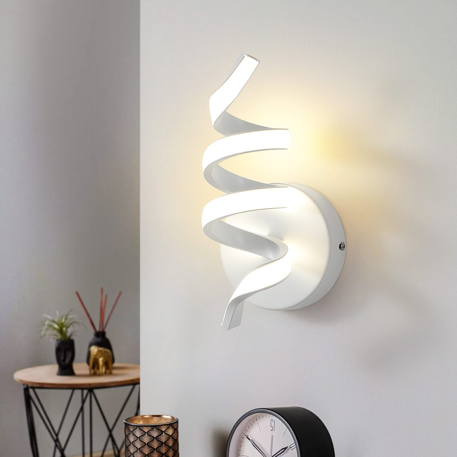 Una moderna lampada da parete a spirale montata su un muro bianco, con tavolo e piante.
