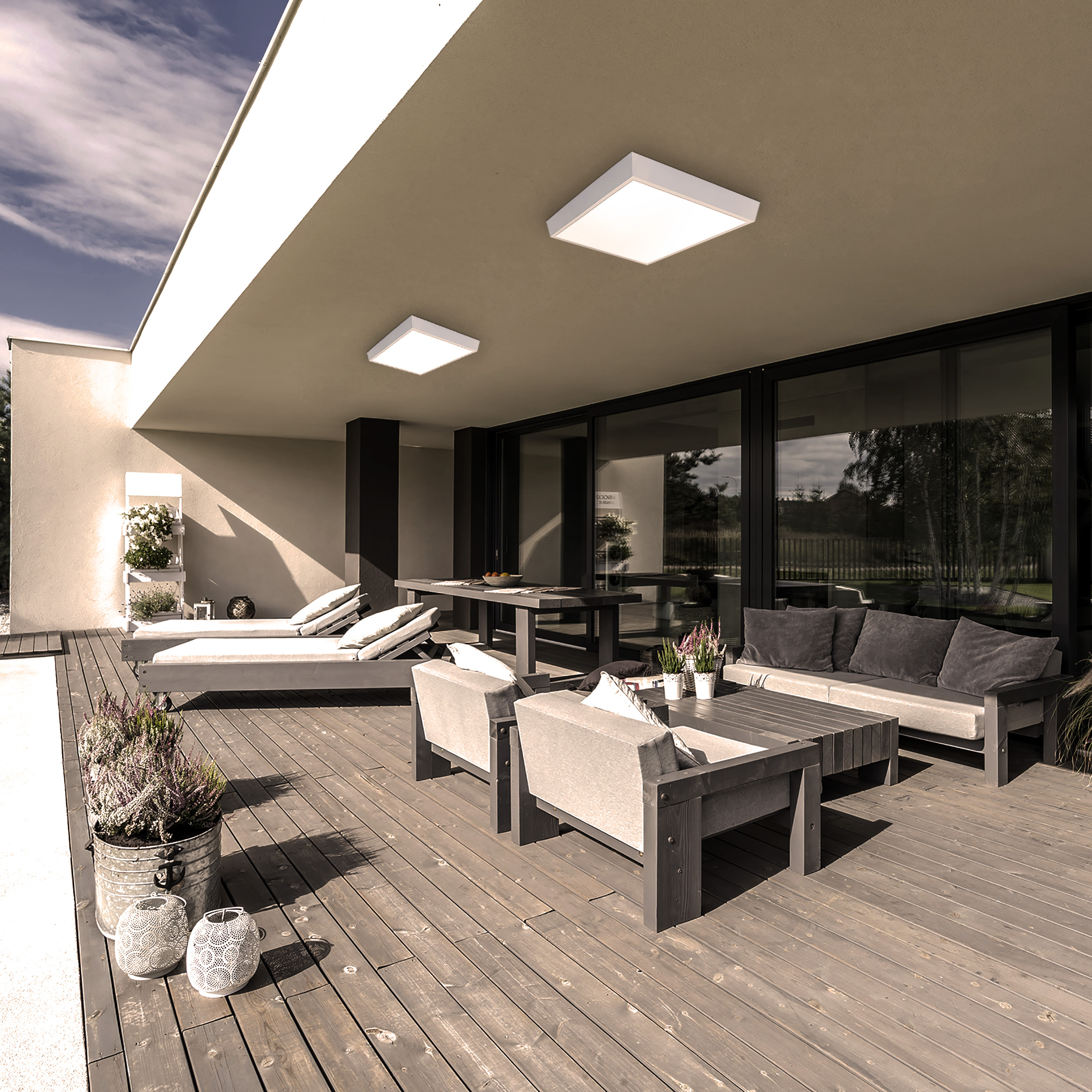 Terrasse mit Holzboden, Sitzgelegenheiten, Tischen und moderner Beleuchtung. Sonniger Tag.