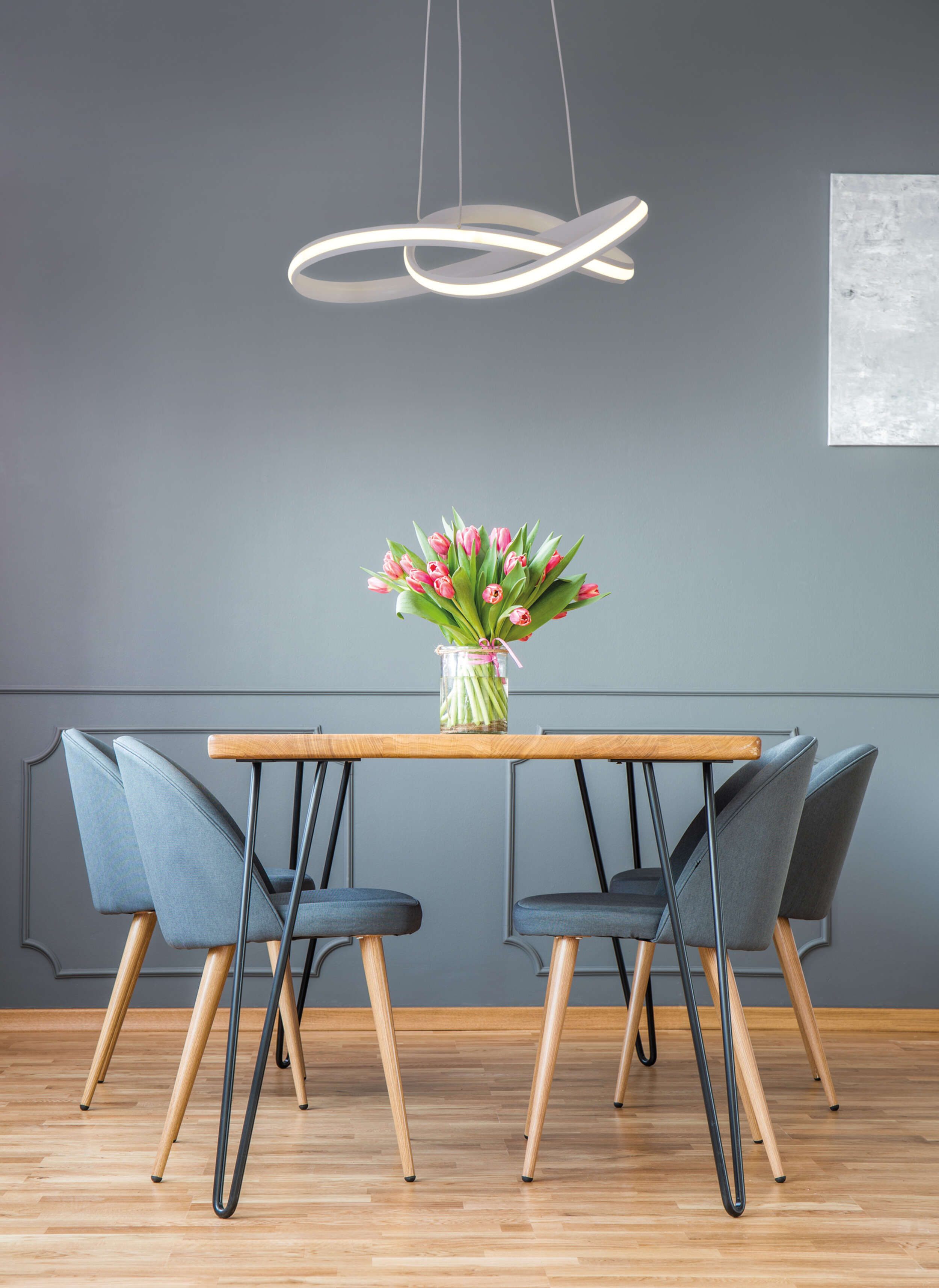 Esszimmer mit Tisch, Blumen und moderner Leuchte darüber.