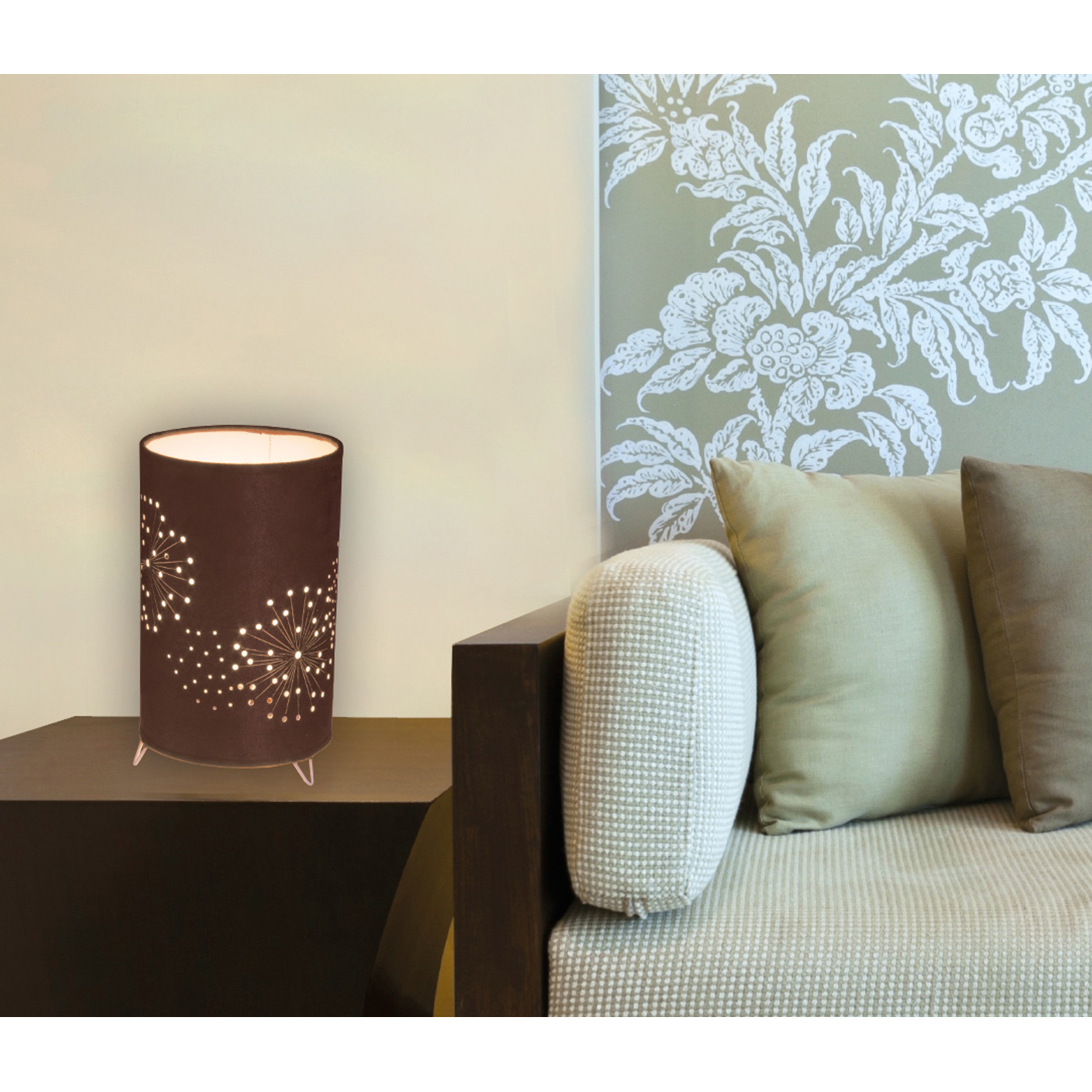 Braune Tischlampe mit floralen Ausschnitten, die Licht auf einen Beistelltisch wirft. Grüne und beige Kissen.