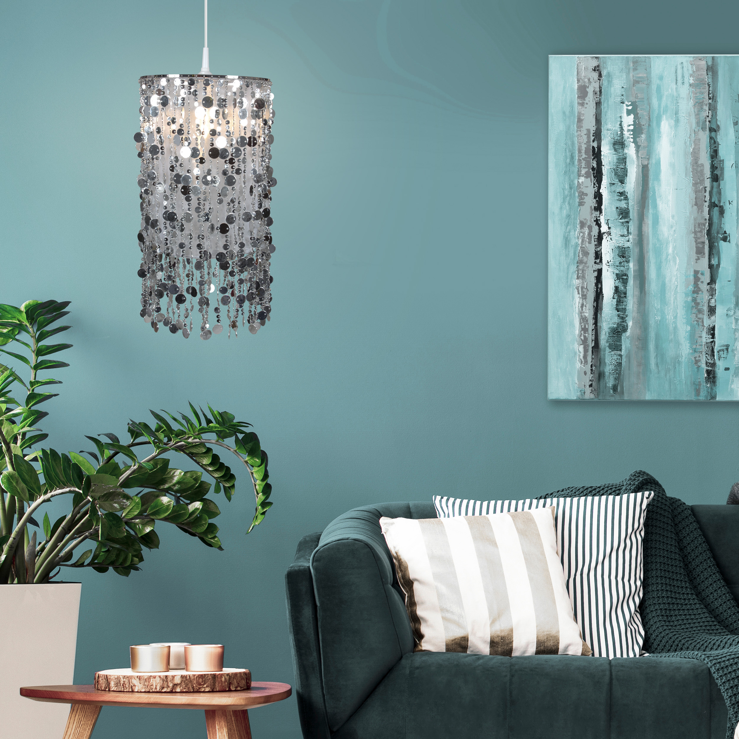 Innenaufnahme mit türkisfarbener Wand, hängender silberner Pendelleuchte und dunkelgrünem Sofa.