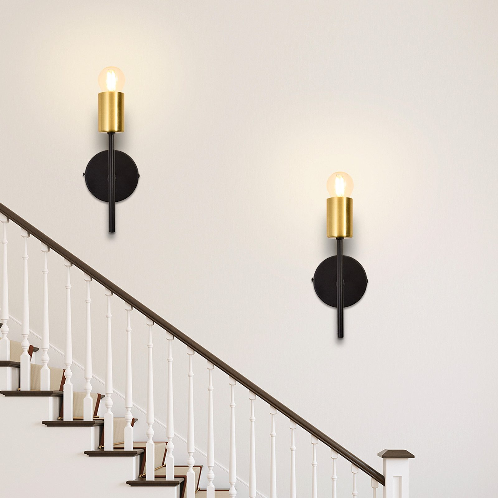 Due applique su un muro bianco. Ognuna ha una base nera e una lampadina color oro.