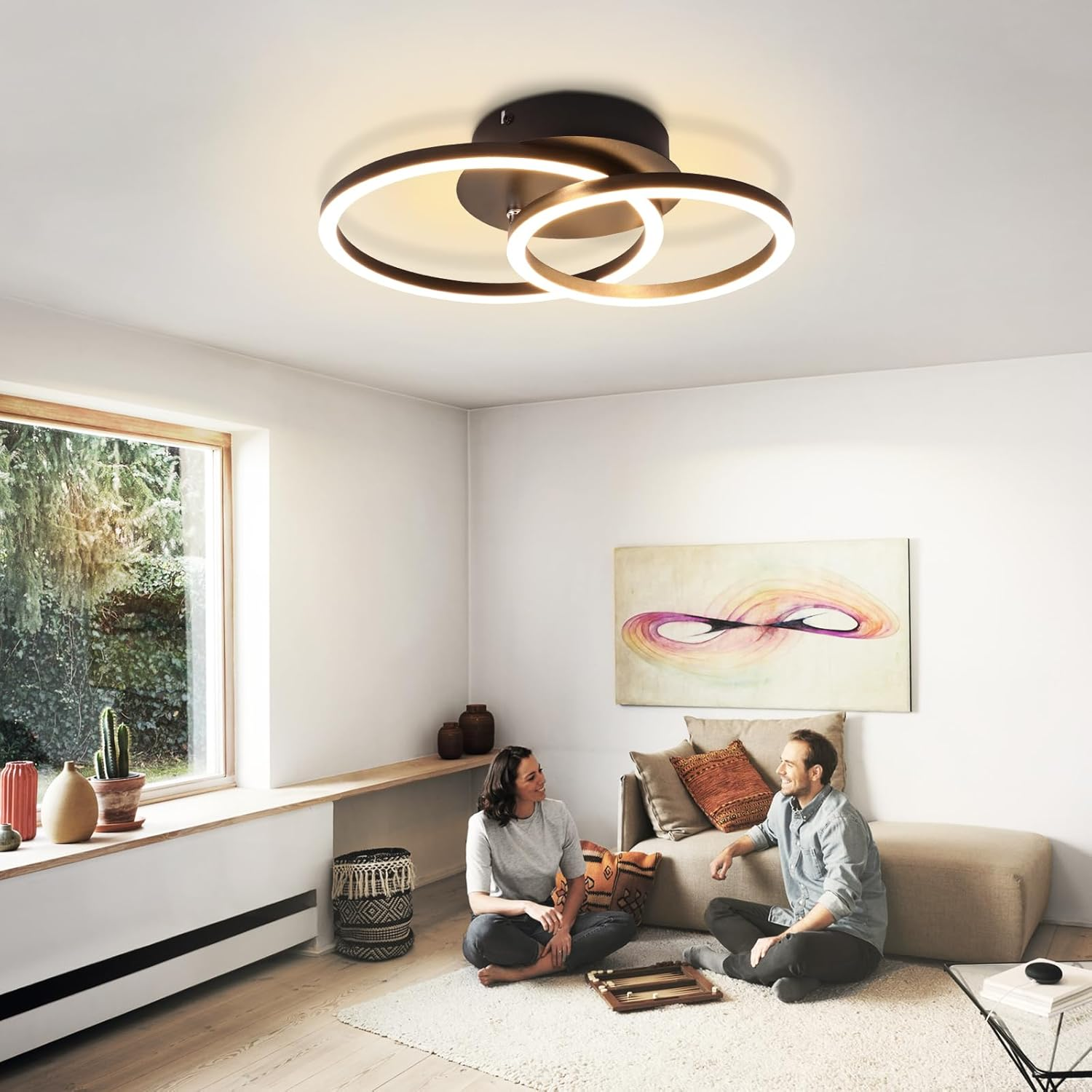 Salón moderno con dos personas sentadas en el suelo, luces de anillo y una ventana.