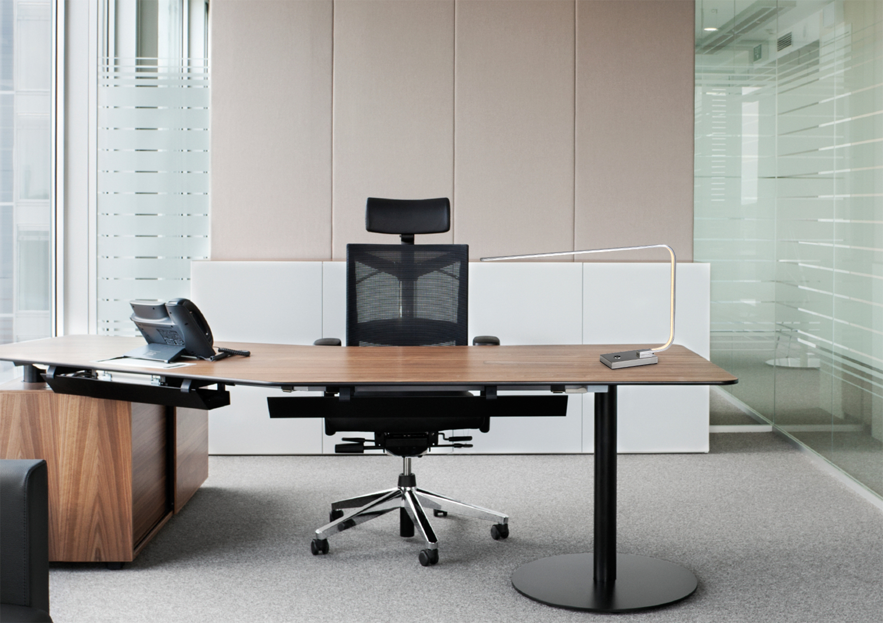 Modernes Büro mit großem Schreibtisch, schwarzem Stuhl und einer schlanken Lampe neben einer Glaswand.