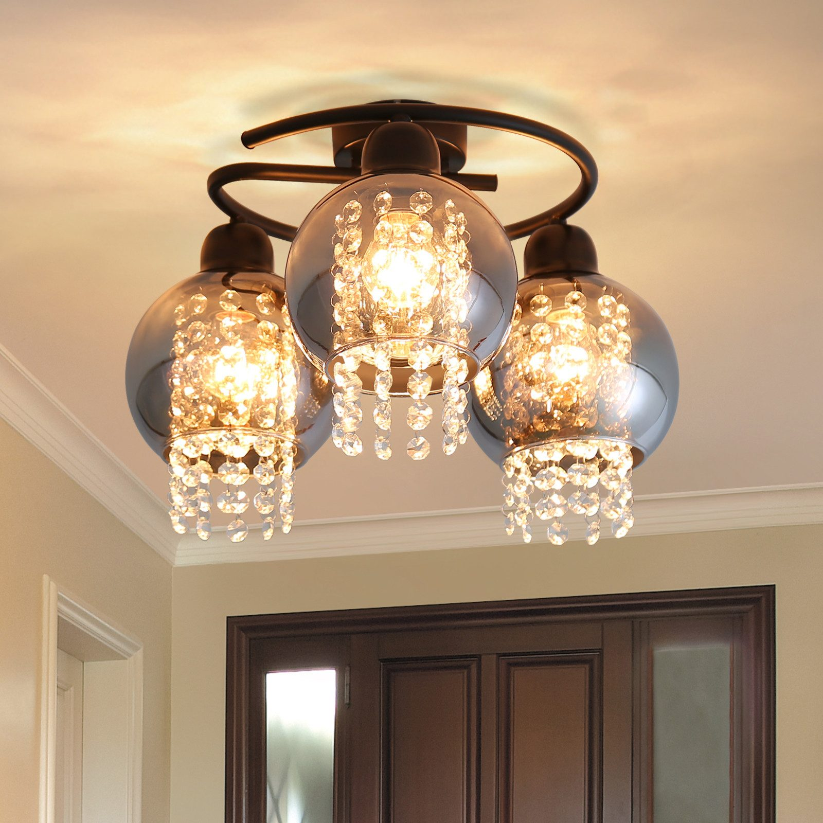 Lampa sufitowa z trzema kulistymi światłami, każda z kryształowymi akcentami, na brązowym suficie.