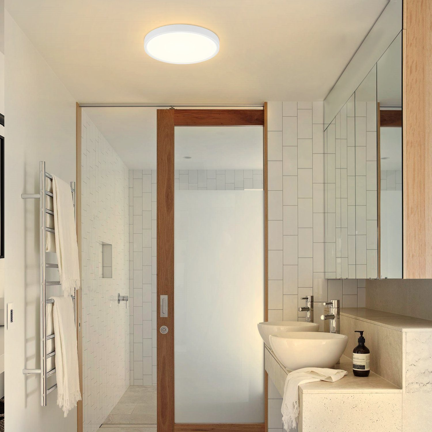 Baño moderno con azulejos blancos, puerta corredera de cristal y luz de techo circular.