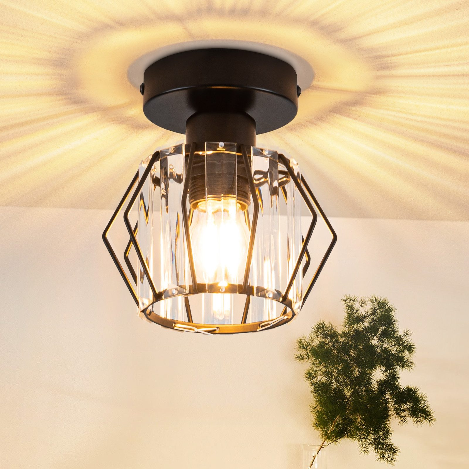 Una luz de techo con diseño geométrico y una bombilla visible, con una planta.