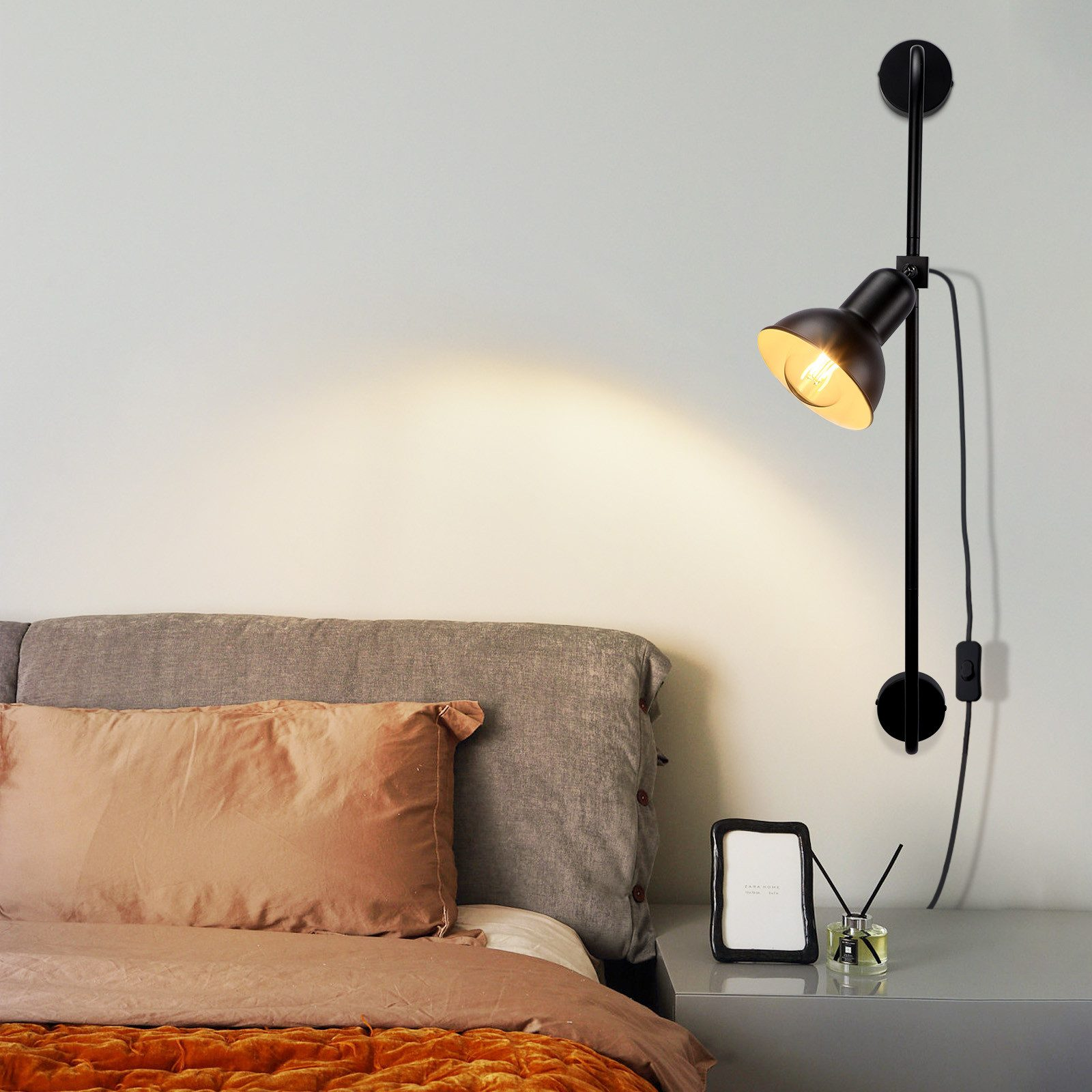 Una lampada da parete nera sopra un letto, che proietta luce su un comodino.