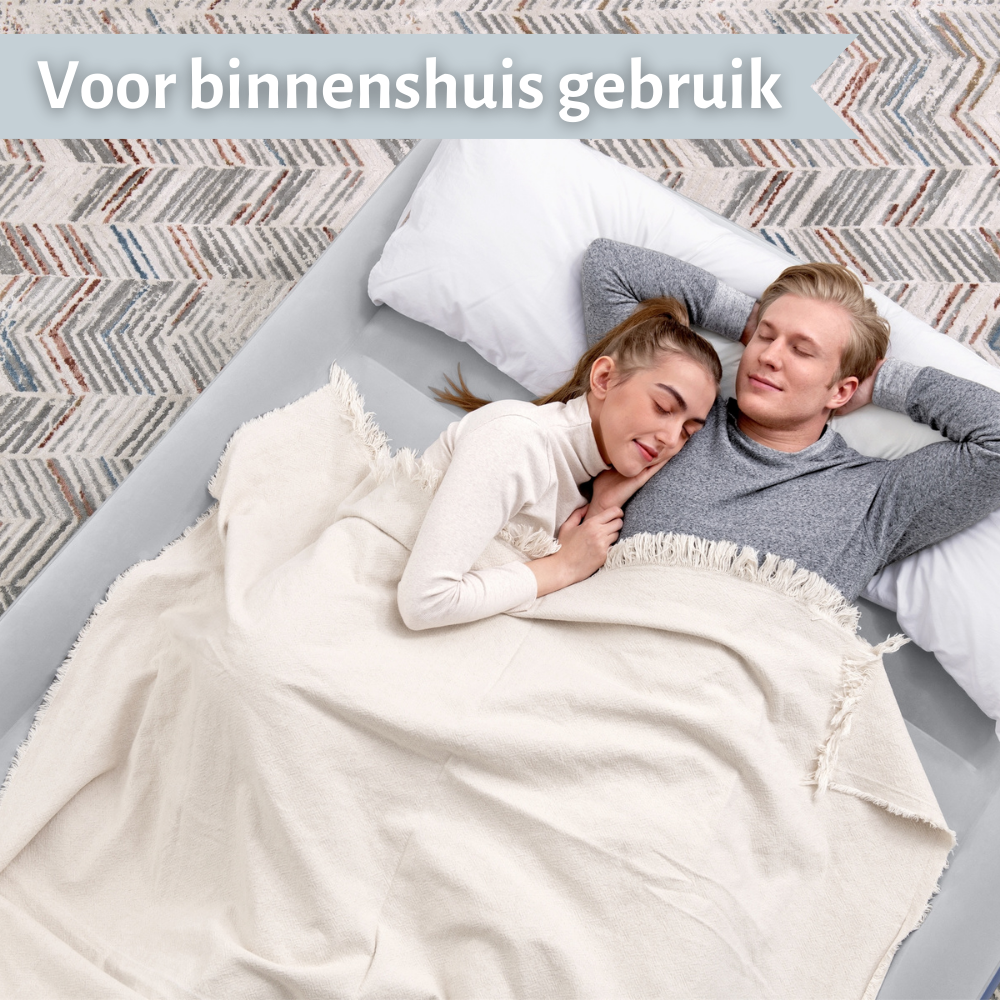Een stel slaapt op een lichtgrijze opblaasmatras in een kamer. Het is bedekt met een crèmekleurige deken.