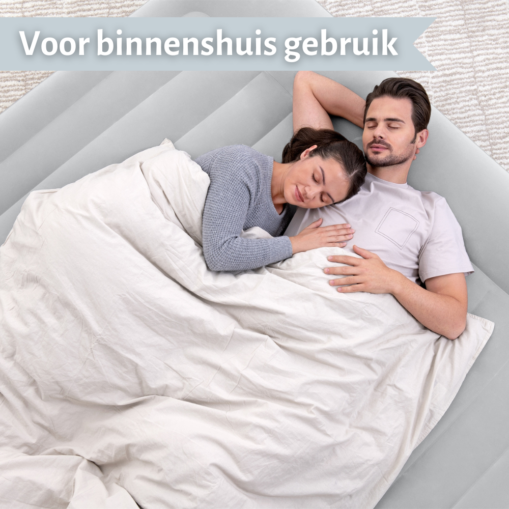 Een stel slaapt op een grijze luchtmatras, bedekt met een deken. De scène is binnenshuis, op een lichtgrijze achtergrond.