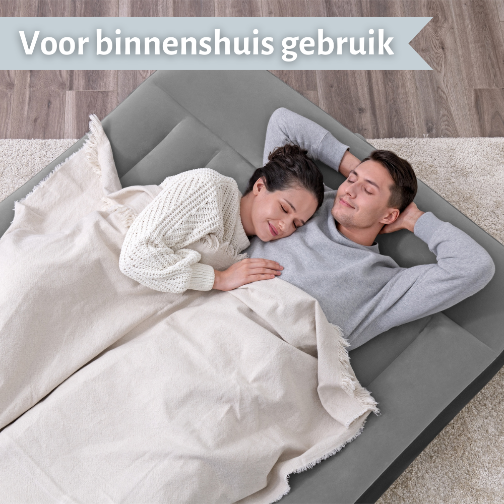 Un couple dort sur un lit gonflable gris, couvert de couvertures. La scène se déroule à l'intérieur sur un tapis.