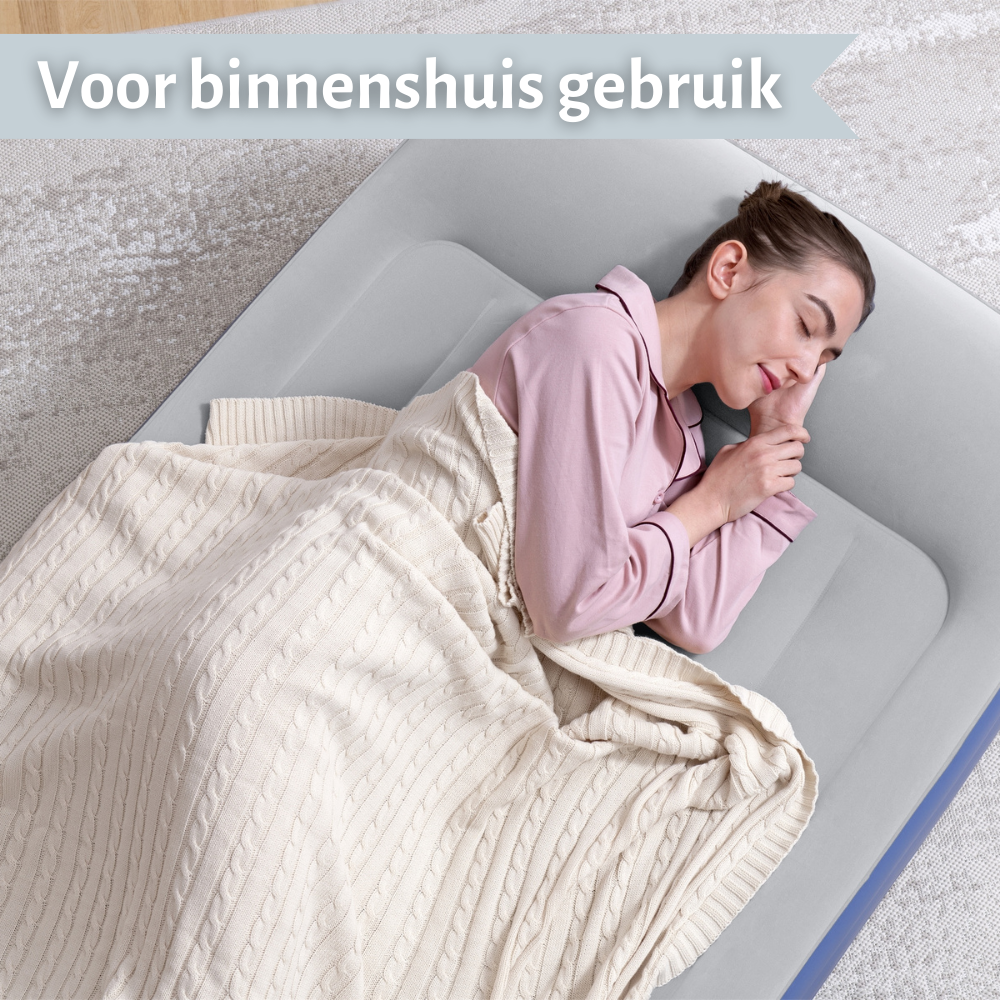 Une femme dort sur un lit gonflable gris, couverte d'une couverture, à l'intérieur sur un tapis.
