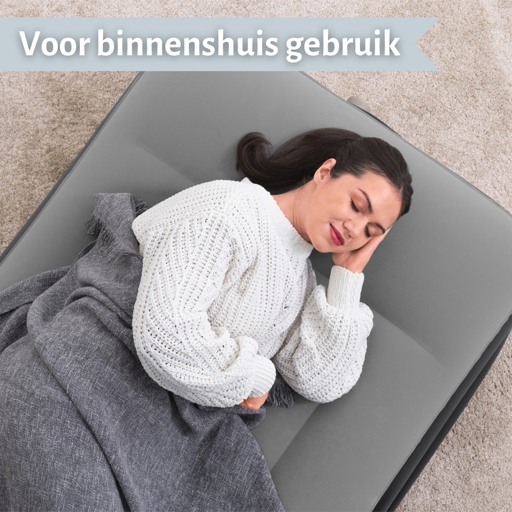 Vrouw ligt op een grijs luchtbed bedekt met een grijze deken. Tekst: Voor binnenshuis gebruik.
