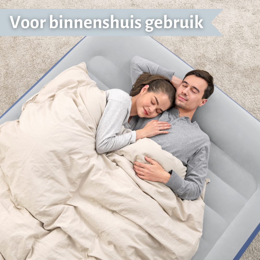 Een stel slaapt op een grijze luchtmatras, bedekt met een deken. De scène is binnenshuis, op een lichtgrijze achtergrond.