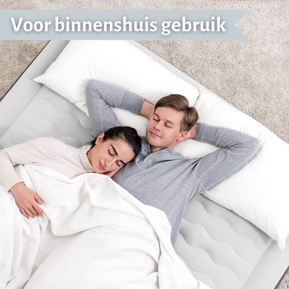 Un couple allongé sur un matelas gonflable gris, couvert d'une couverture blanche, avec des oreillers. Ils ont l'air détendus.