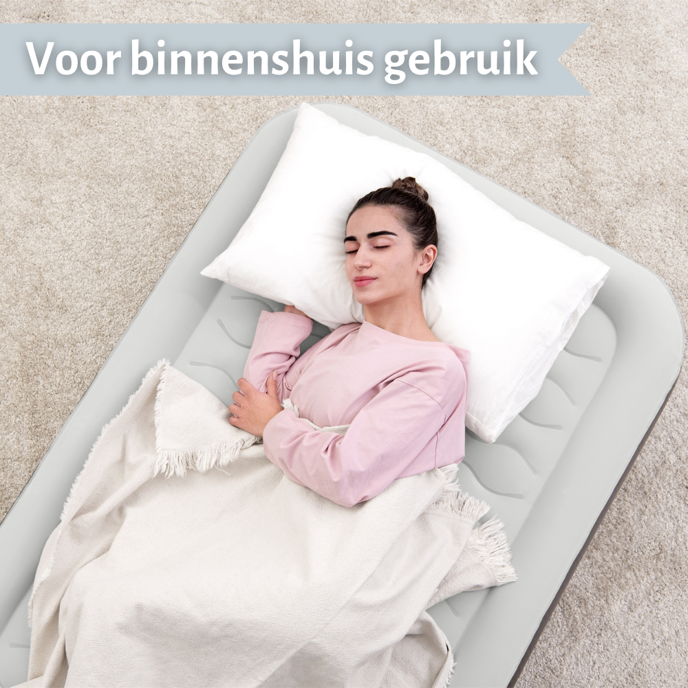 Een vrouw slaapt op een grijs luchtbed met een wit kussen en deken. Tekst: "Voor gebruik binnenshuis".