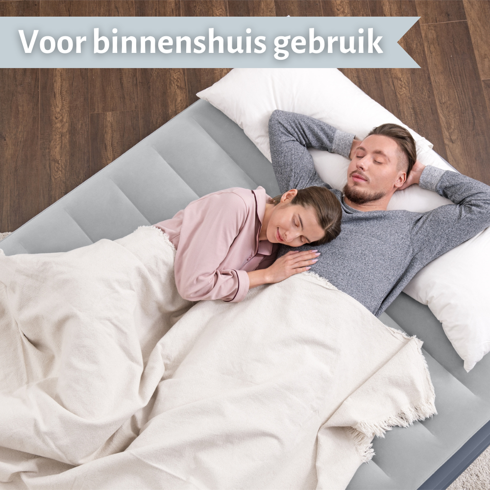 Een stel slaapt op een grijs luchtbed, met kussens en een witte deken.