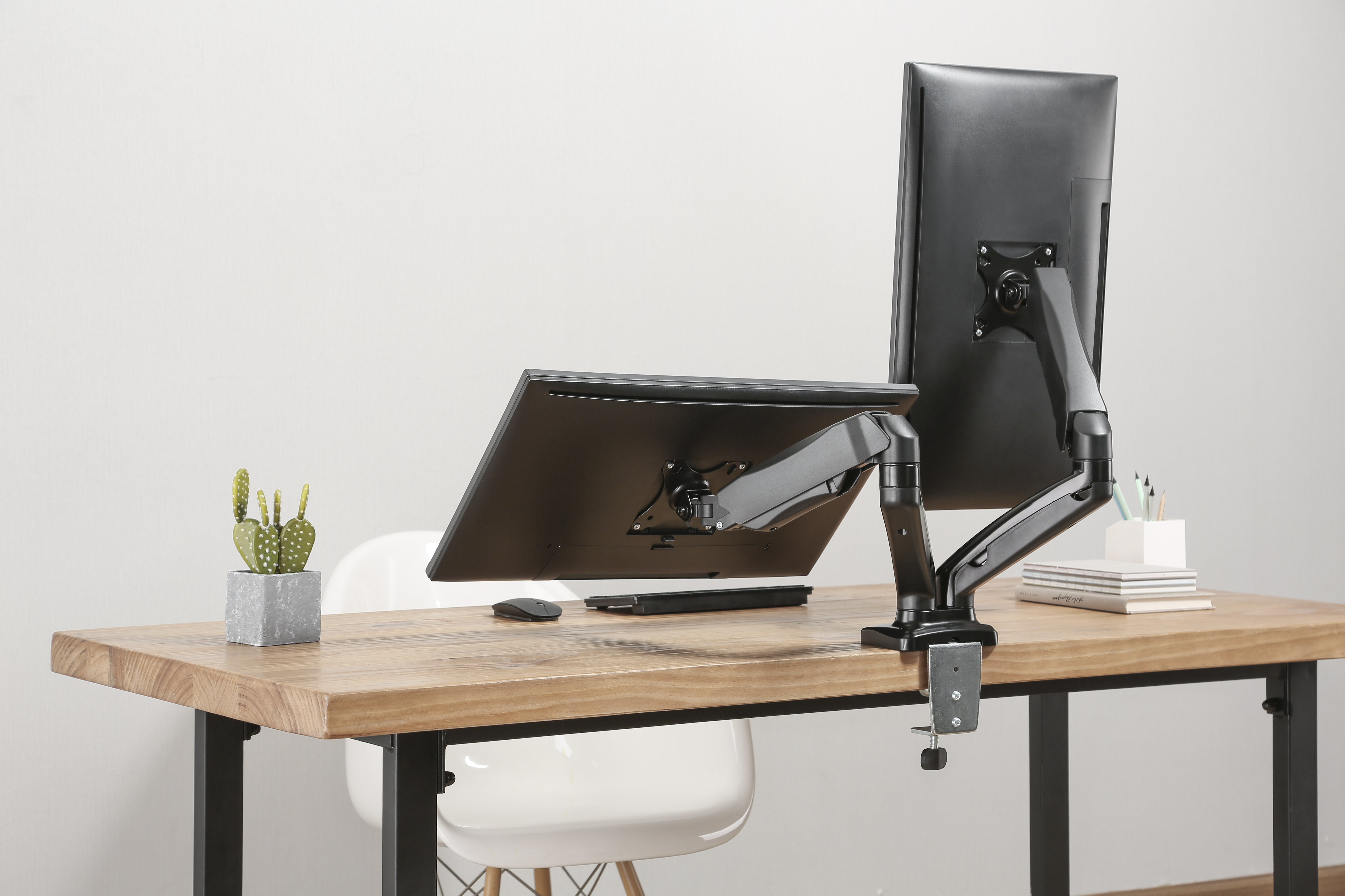 Monitor und Laptop auf einem Schreibtisch mit Monitorarm. Weiße Wand im Hintergrund.