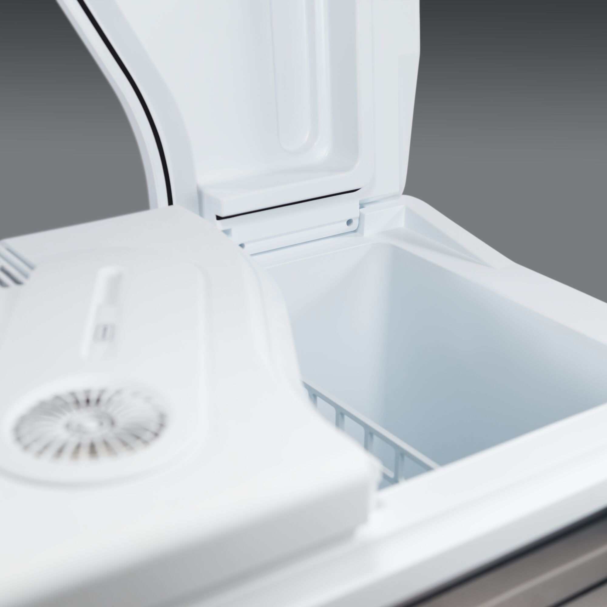 Frigorifero bianco aperto con coperchio socchiuso. All'interno c'è una griglia di filo bianco. Sfondo grigio.