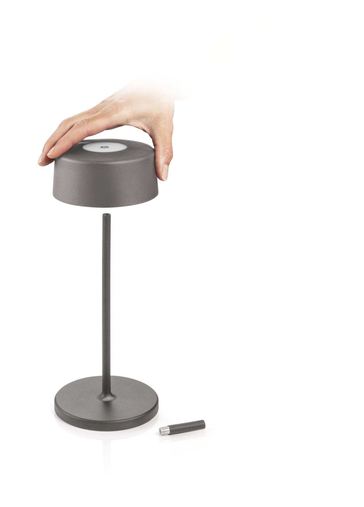 Eine Hand platziert einen Lampenkopf auf dem Sockel. Die Lampe ist dunkelgrau, der Sockel kreisförmig.