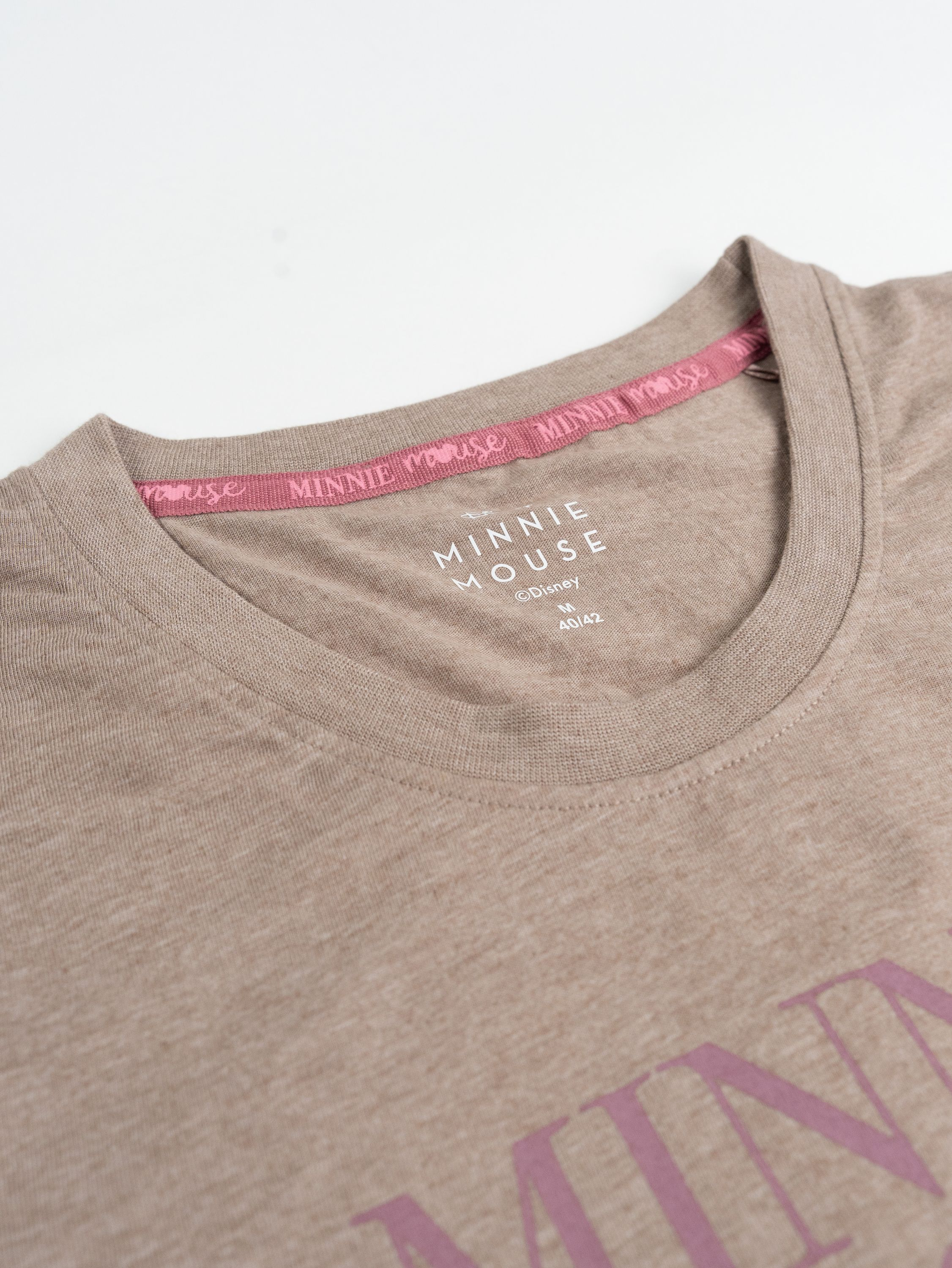 Beige Minnie Mouse T-Shirt. Pinker Schriftzug und Kragenbesatz. Weißer Hintergrund.