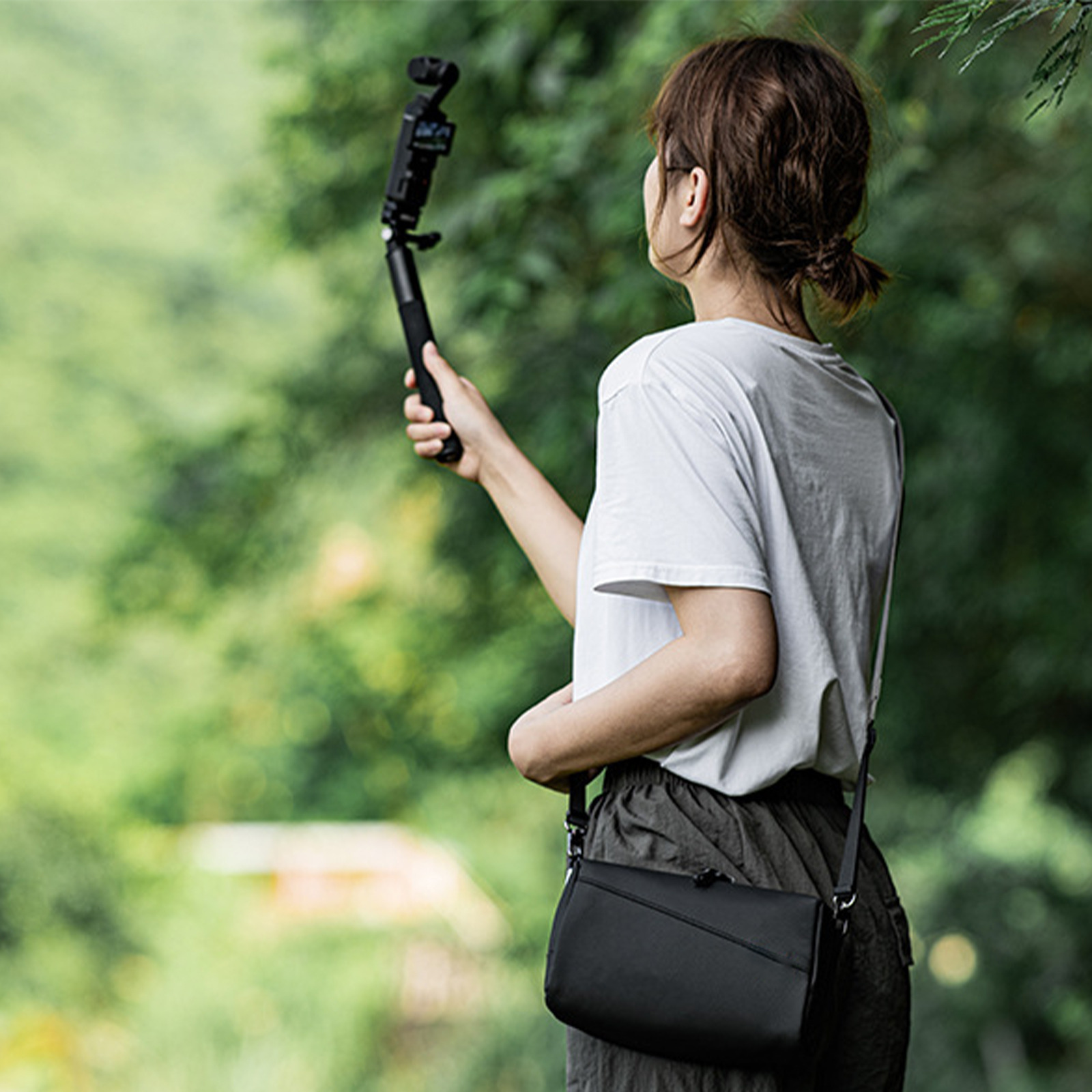 Eine Frau, die eine Kamera auf einem Stativ hält, trägt ein weißes Hemd und eine schwarze Tasche.