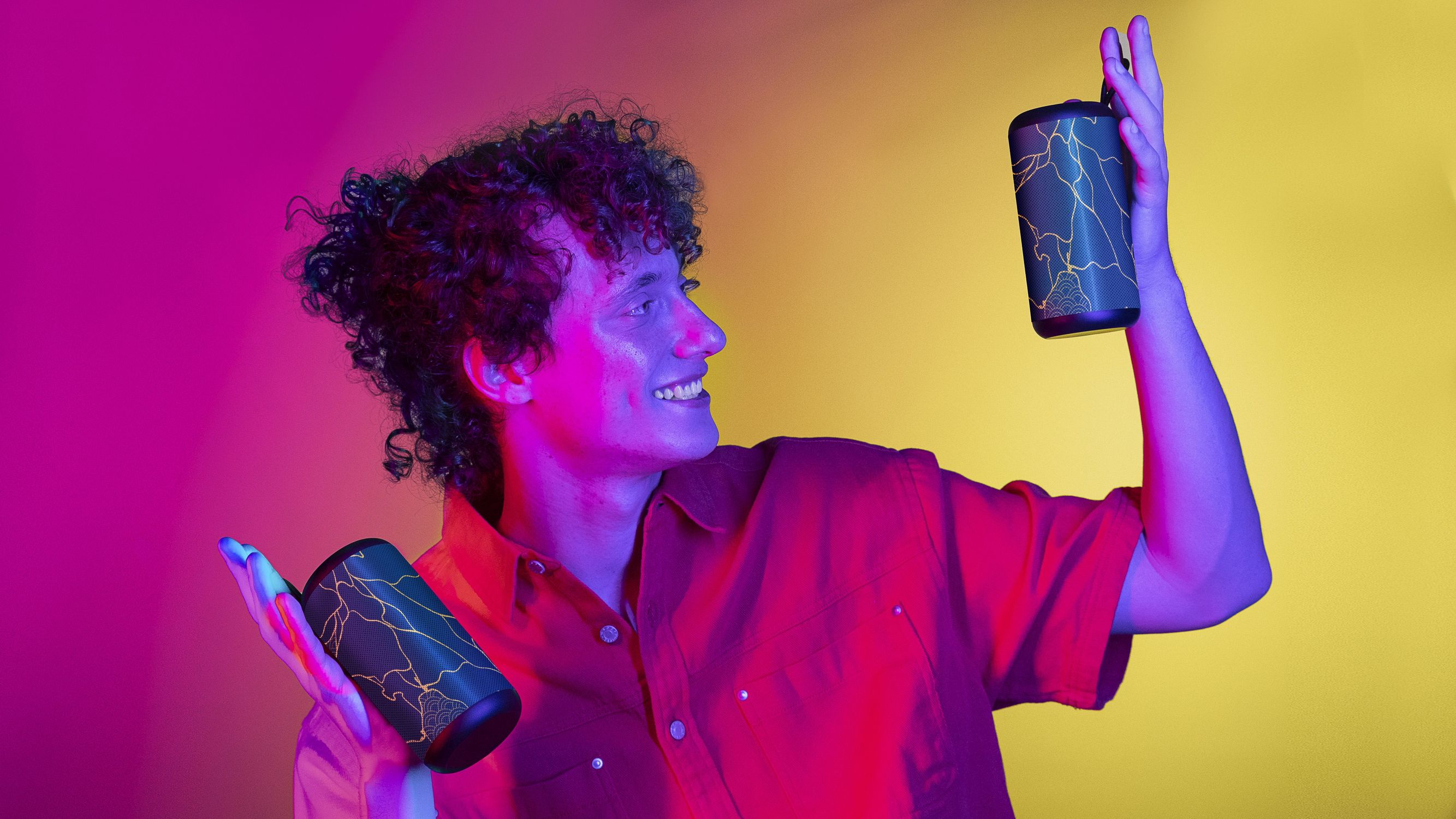 Mężczyzna trzymający dwa głośniki. Tło ma kolory różowy, fioletowy i żółty.