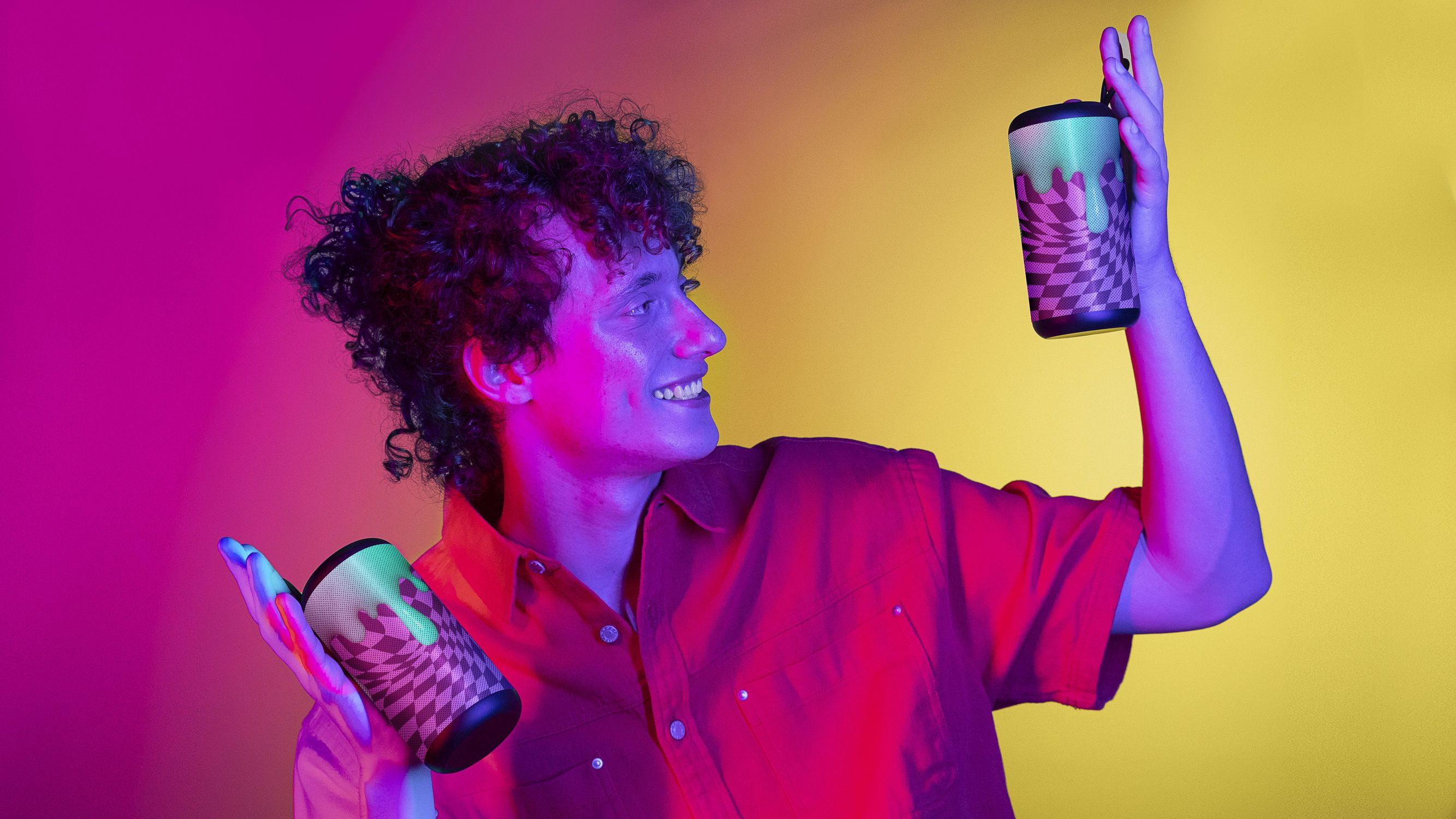 Mężczyzna trzyma dwa głośniki. Tło ma gradient żółto-fioletowy.