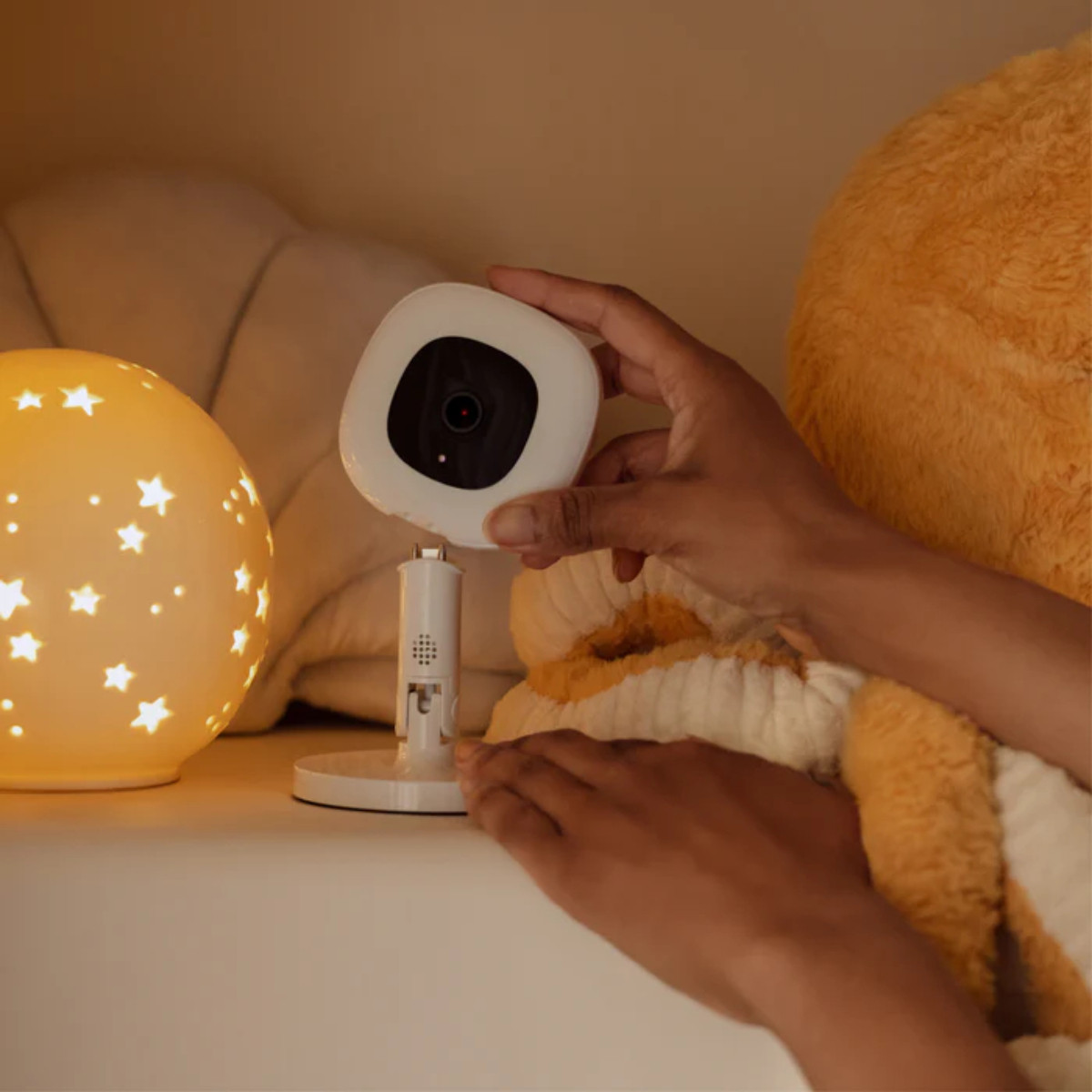 Eine Hand stellt eine weiße Babyüberwachungskamera auf einem Ständer ein, mit einem sternförmigen Licht im Hintergrund.