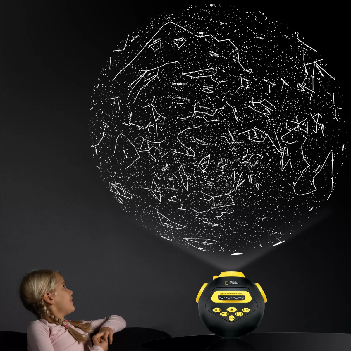 Una ragazza guarda un cielo stellato proiettato su un muro da un proiettore National Geographic.