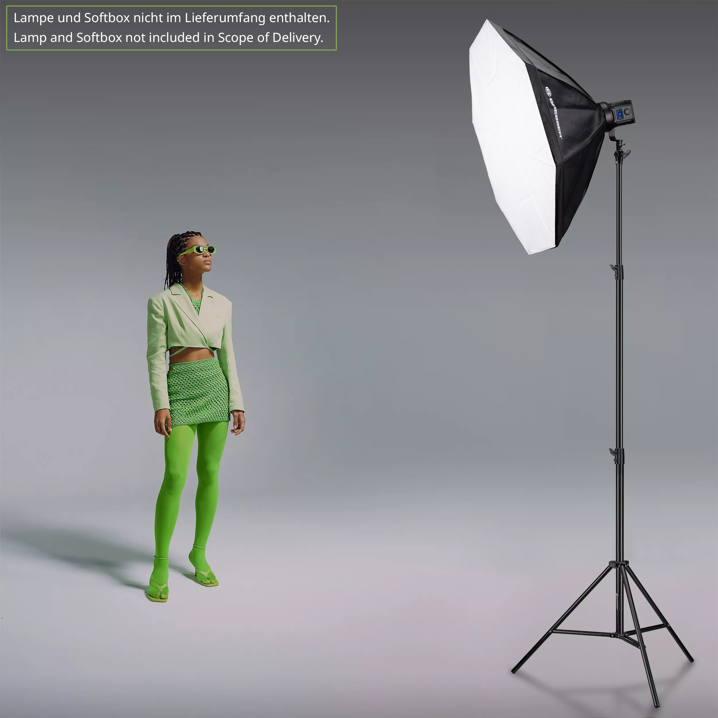 Vrouw in groene outfit, zonnebril, in de buurt van een grote studiolamp op een statief.