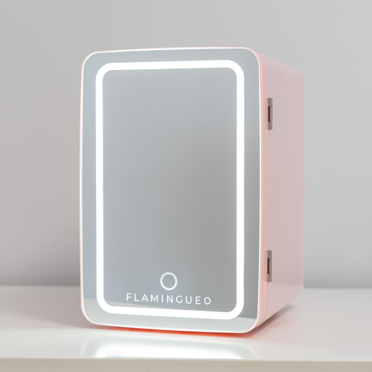 Mini nevera rosa con puerta de espejo y luces LED, colocada sobre una mesa blanca.