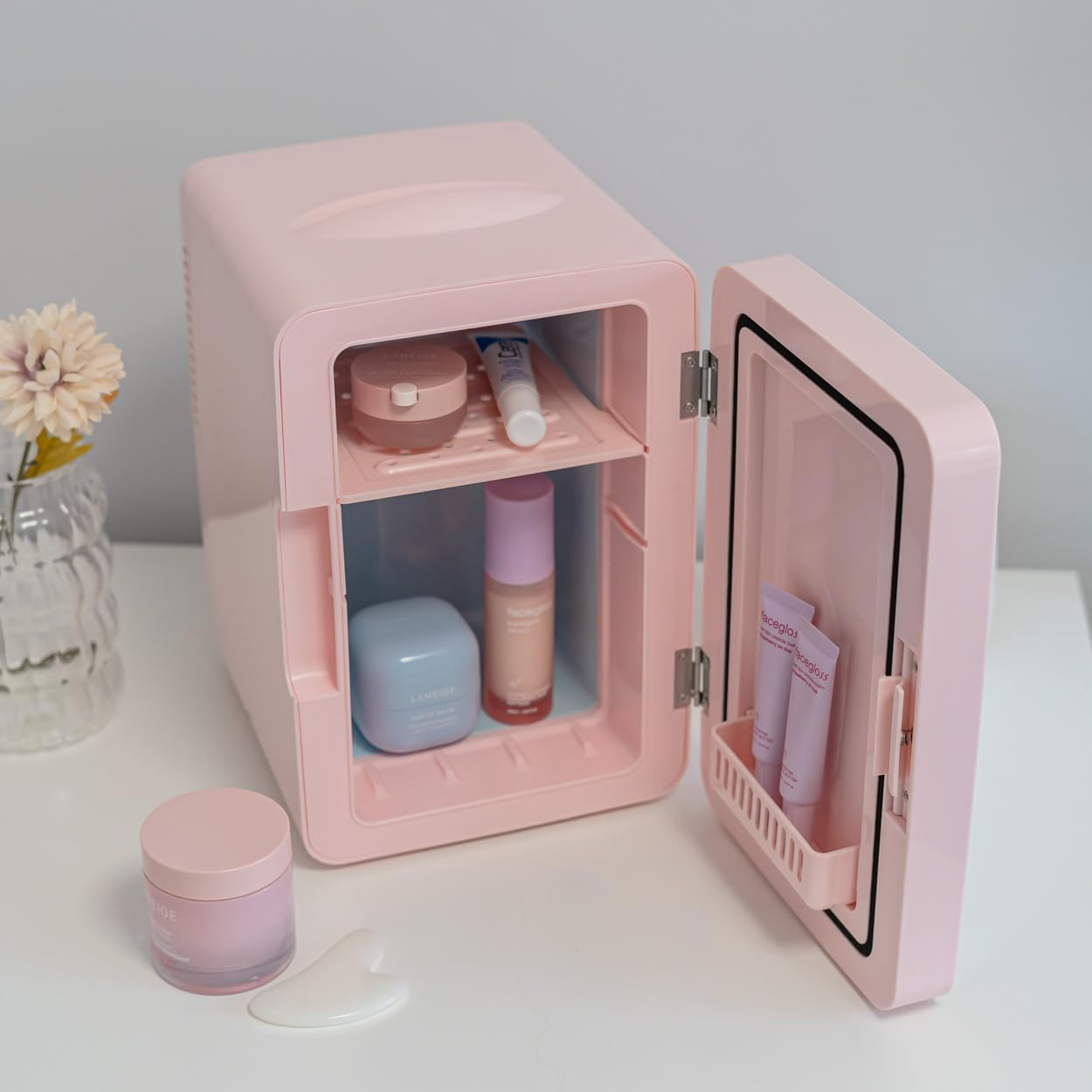 Mini-nevera rosa con productos para el cuidado de la piel dentro y en la mesa auxiliar.