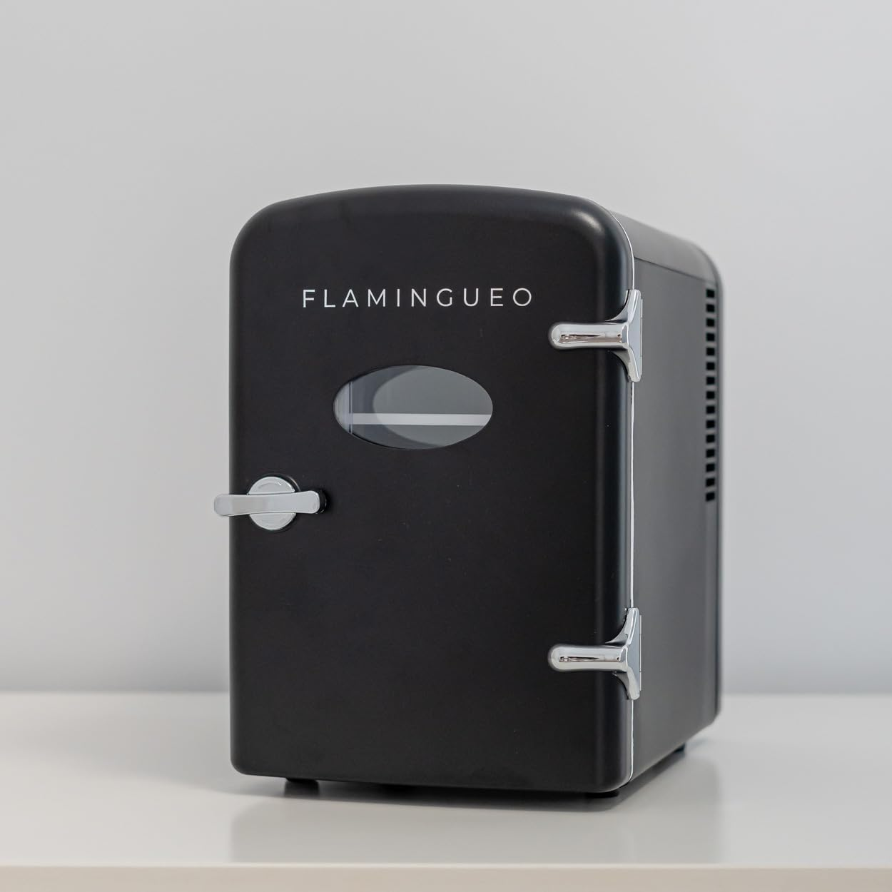 Un pequeño refrigerador negro con la palabra 'FLAMINGUEO'. Tiene una pequeña ventana en la puerta.