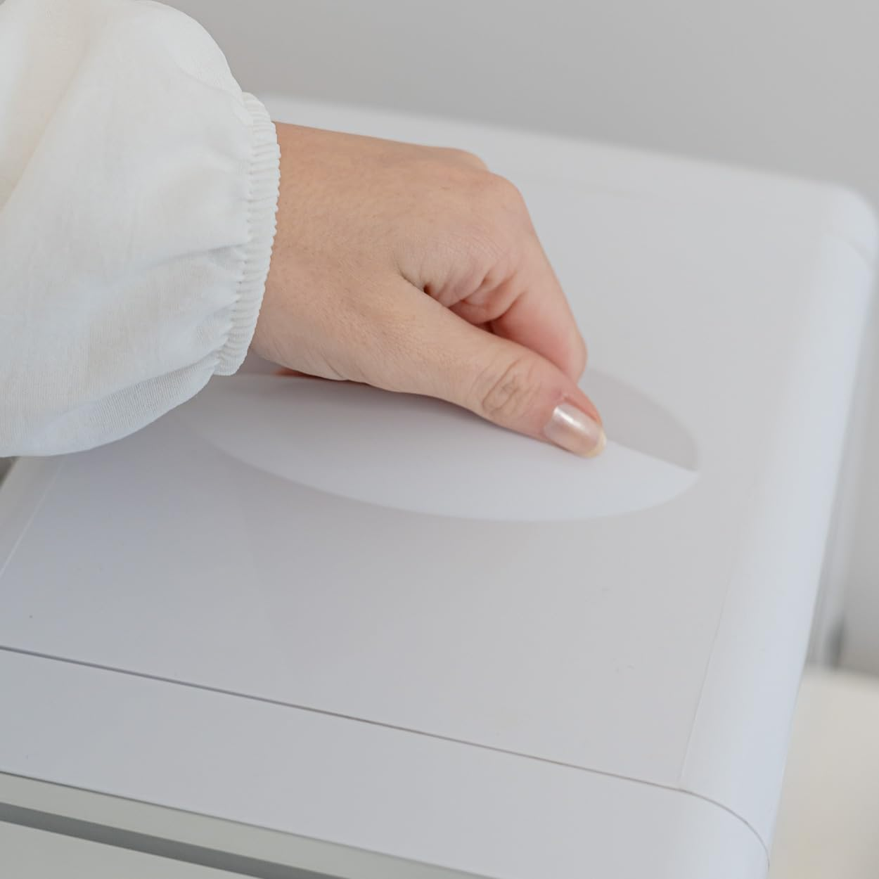 Una mano abriendo un dispositivo blanco. El foco está en la mano y la superficie.