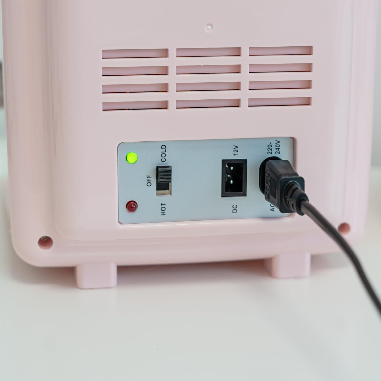 Una mini-nevera rosa con botones de encendido y un cable de alimentación enchufado.
