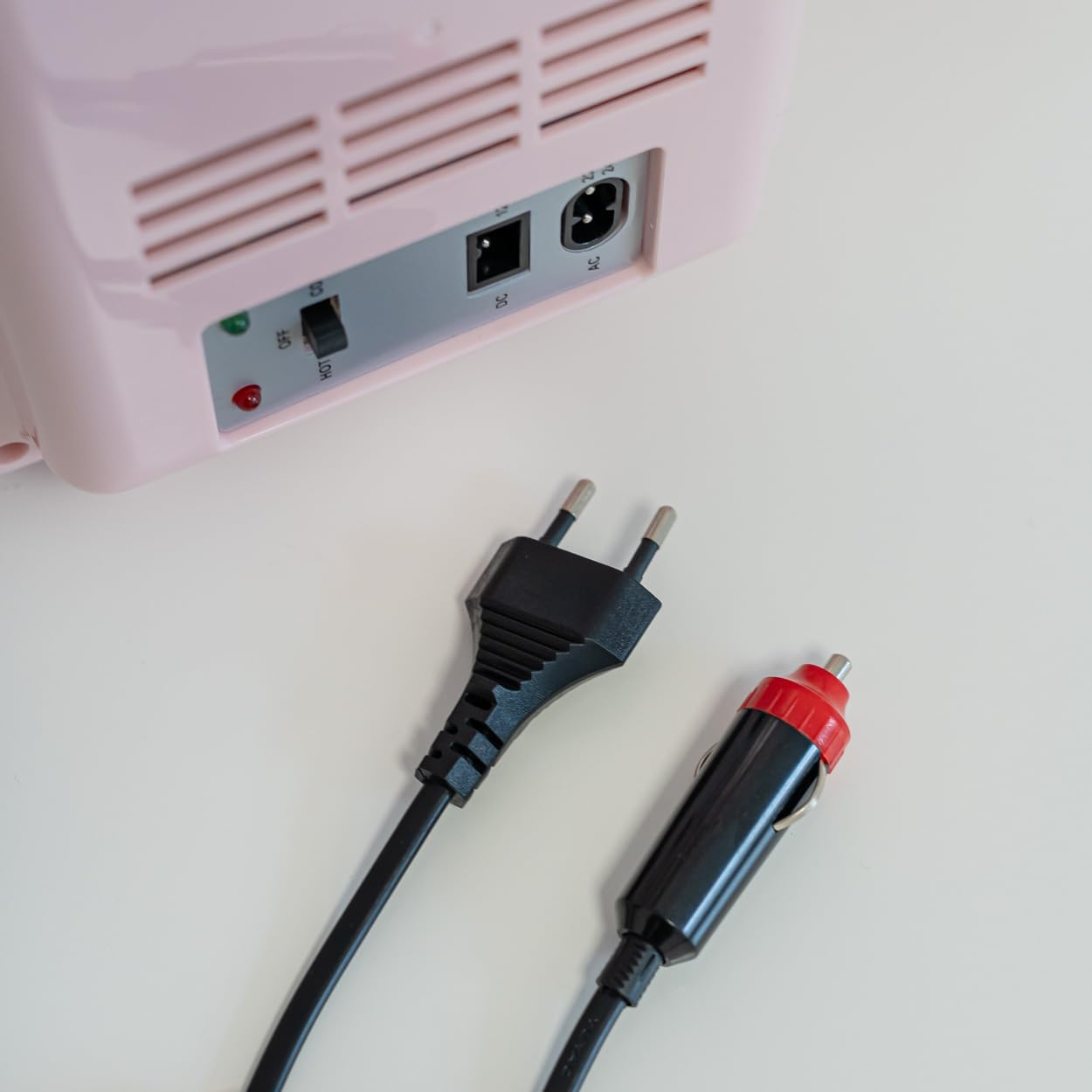 Mini nevera rosa con dos cables de alimentación. Un enchufe negro y un enchufe de cargador de coche.