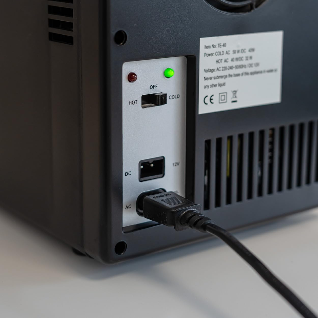 Parte trasera de mini-nevera negra. Cable de alimentación enchufado. Controles: interruptor caliente/frío y entrada de energía.
