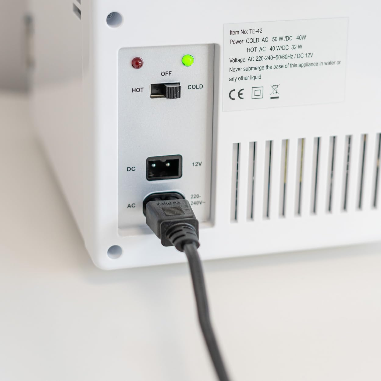 Parte trasera de una mini nevera blanca, mostrando interruptor, puertos AC/DC y cable de alimentación negro.